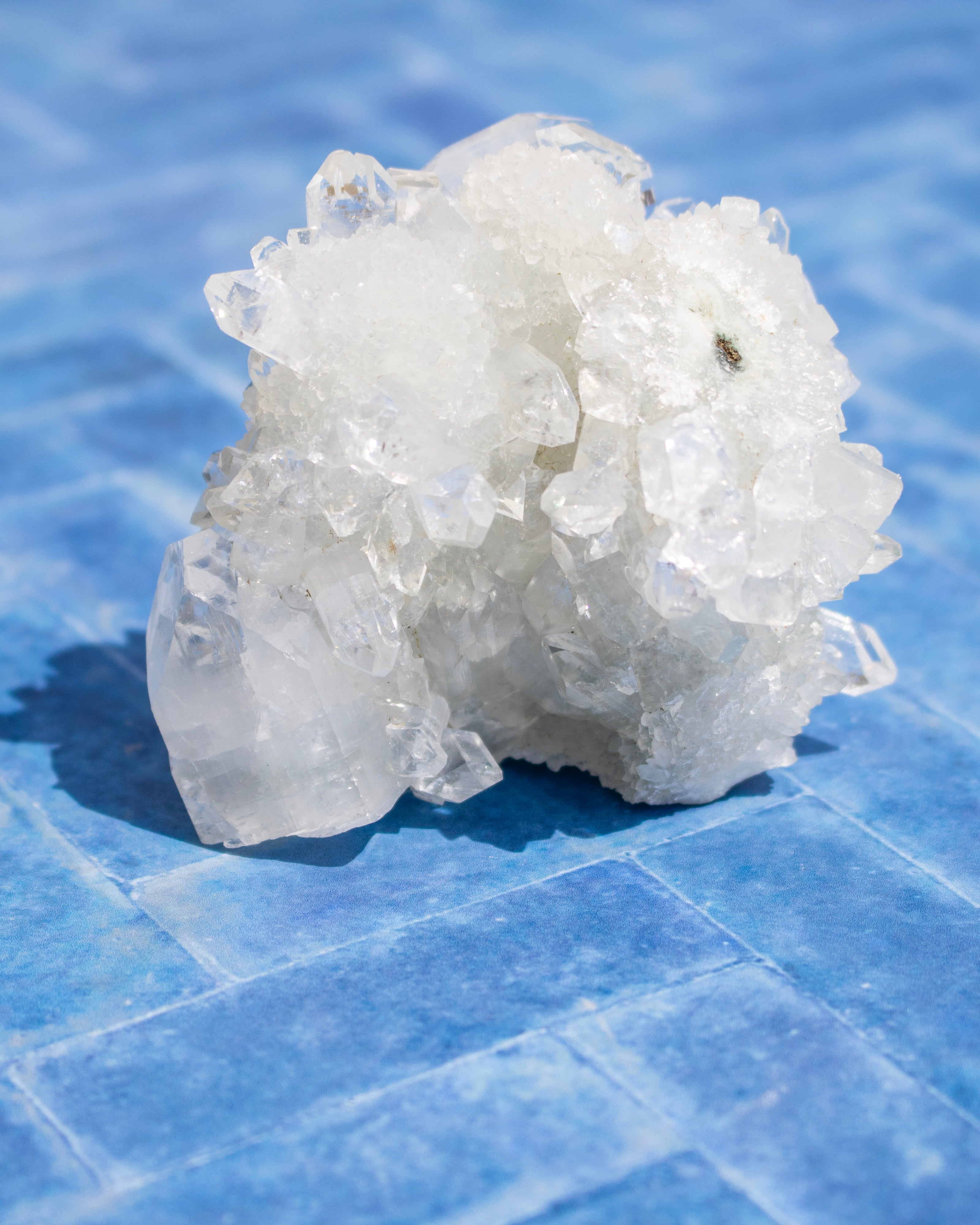 A cluster of translucent white crystals with a rough, natural texture, resting on a blue tiled surface.