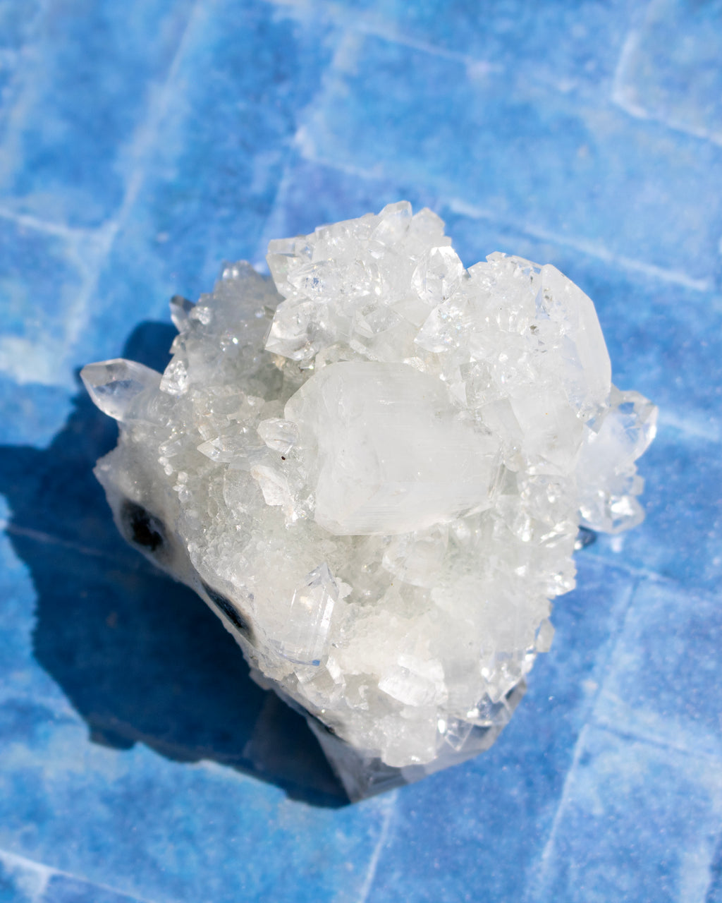A cluster of white quartz crystals with natural rough edges, resting on a textured blue surface.