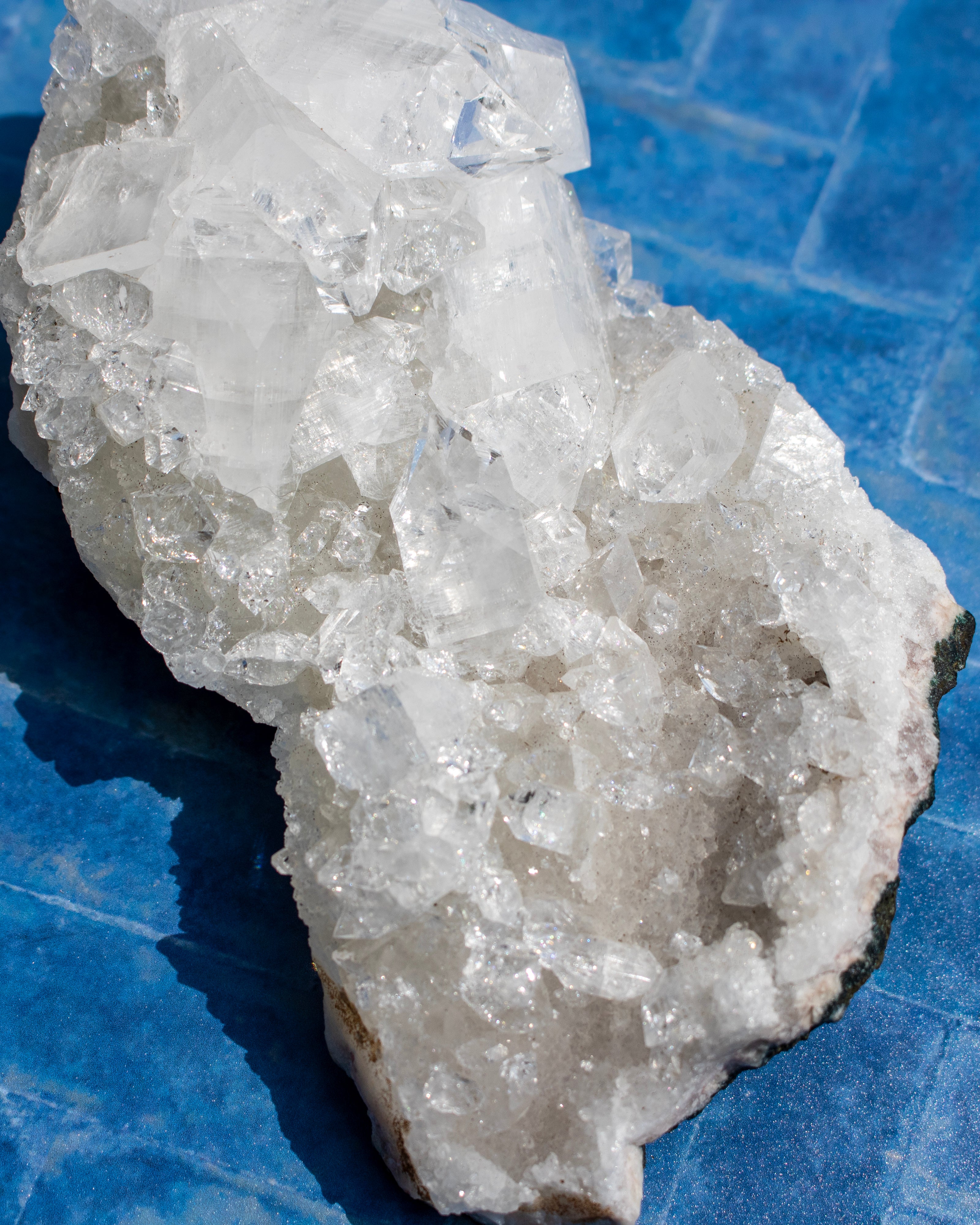 A raw crystal cluster with translucent white and clear quartz-like formations resting on a bright blue tiled surface.
