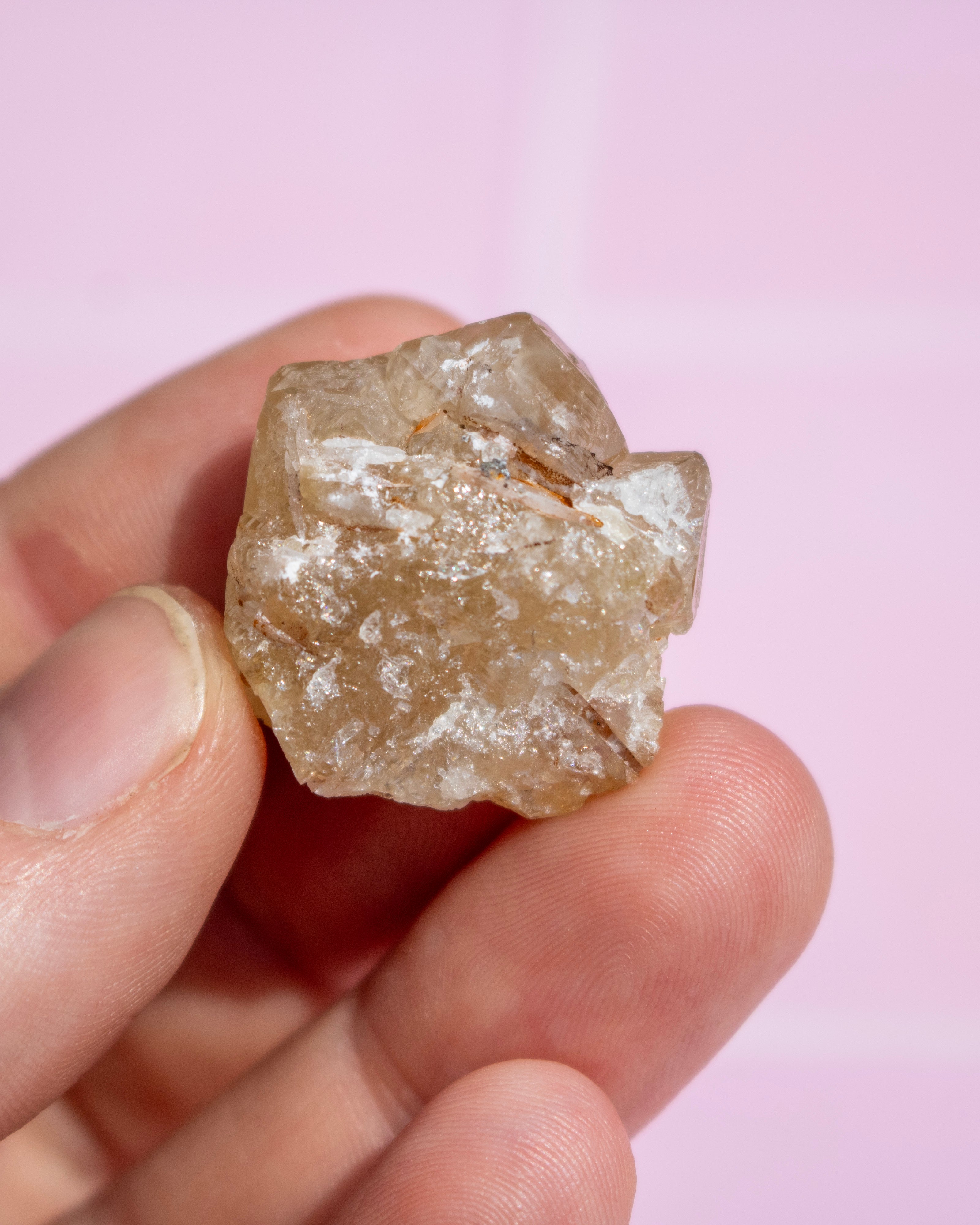 A rough, unpolished crystal or mineral specimen held between fingers against a soft pink background.