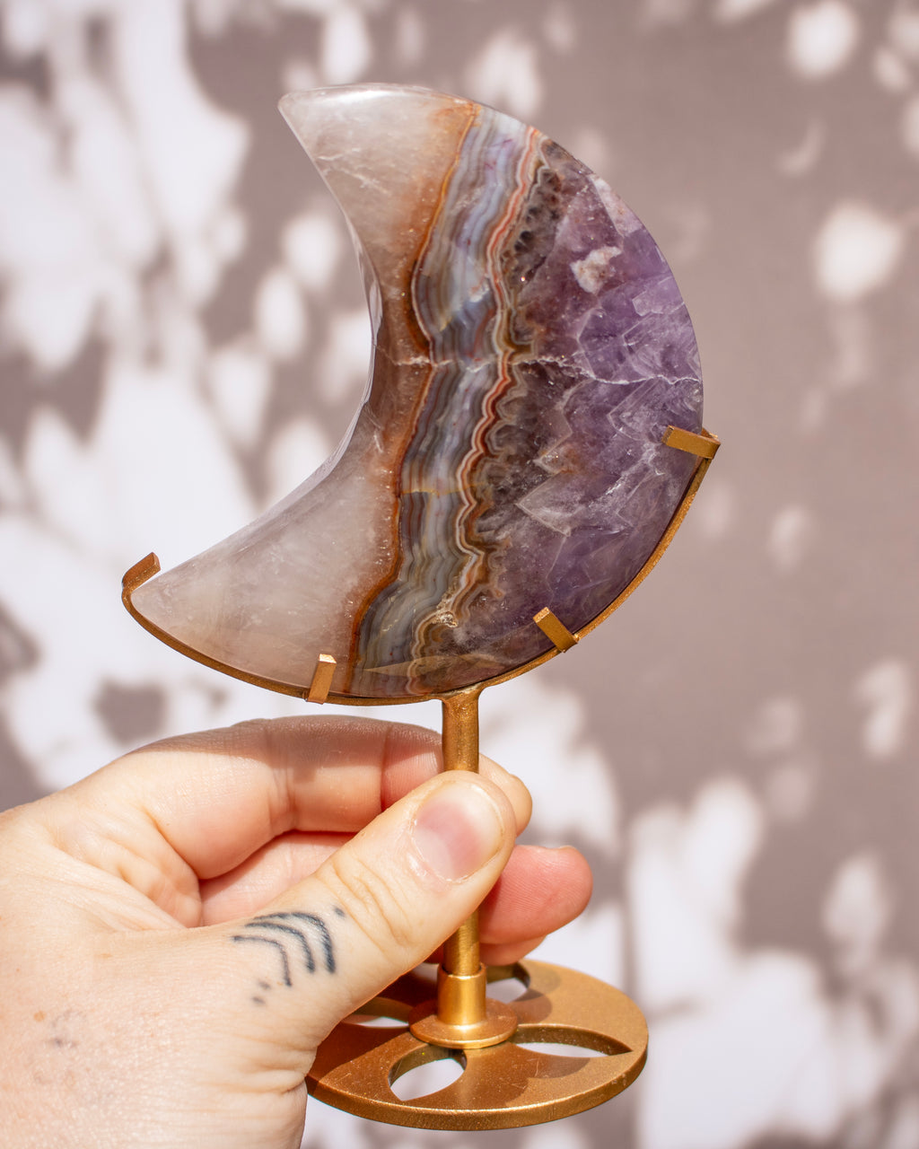 A hand holds a polished crescent moon-shaped agate geode specimen on a brass stand against a soft shadowed background.