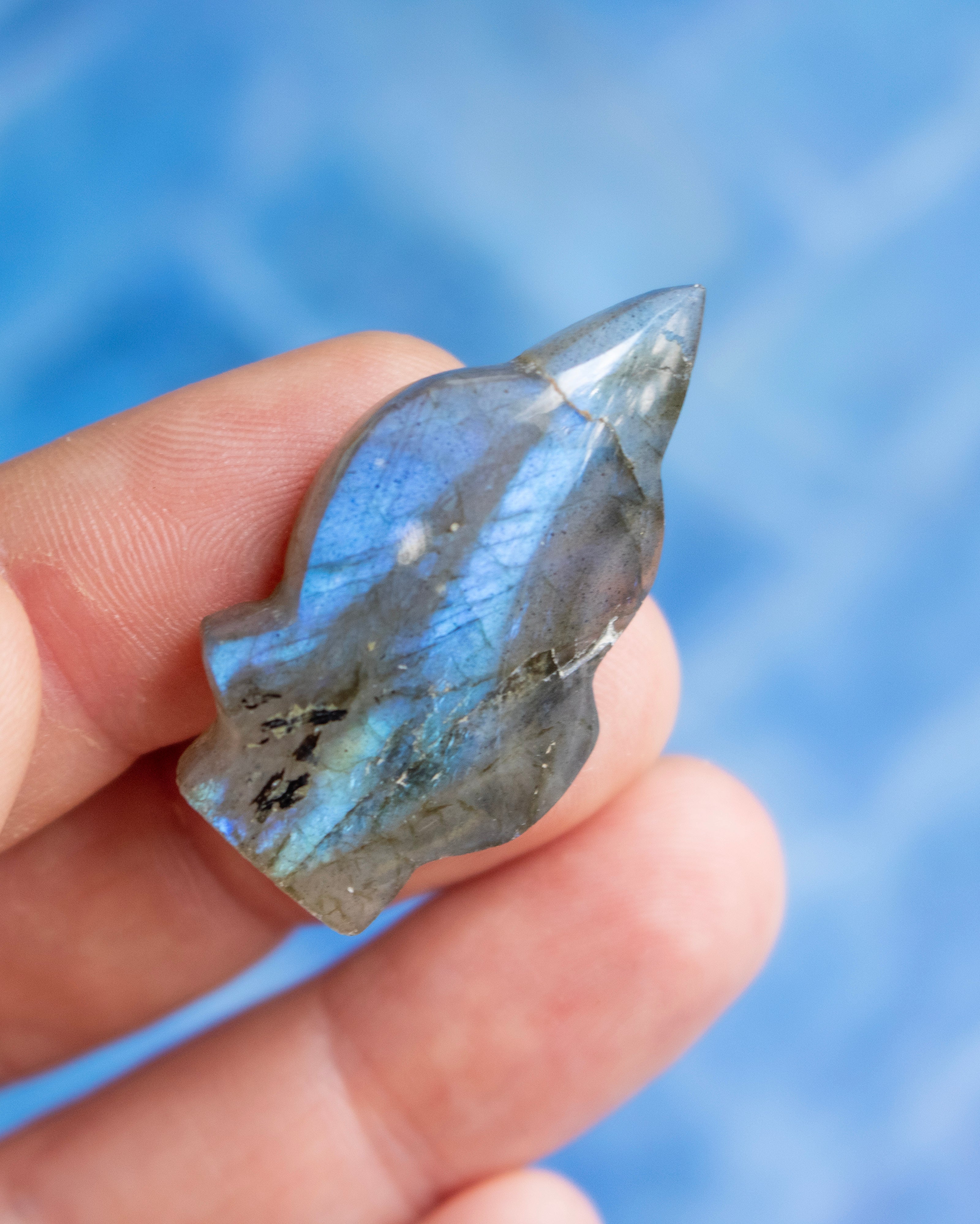 A hand holding a polished labradorite crystal point against a soft blue blurred background.