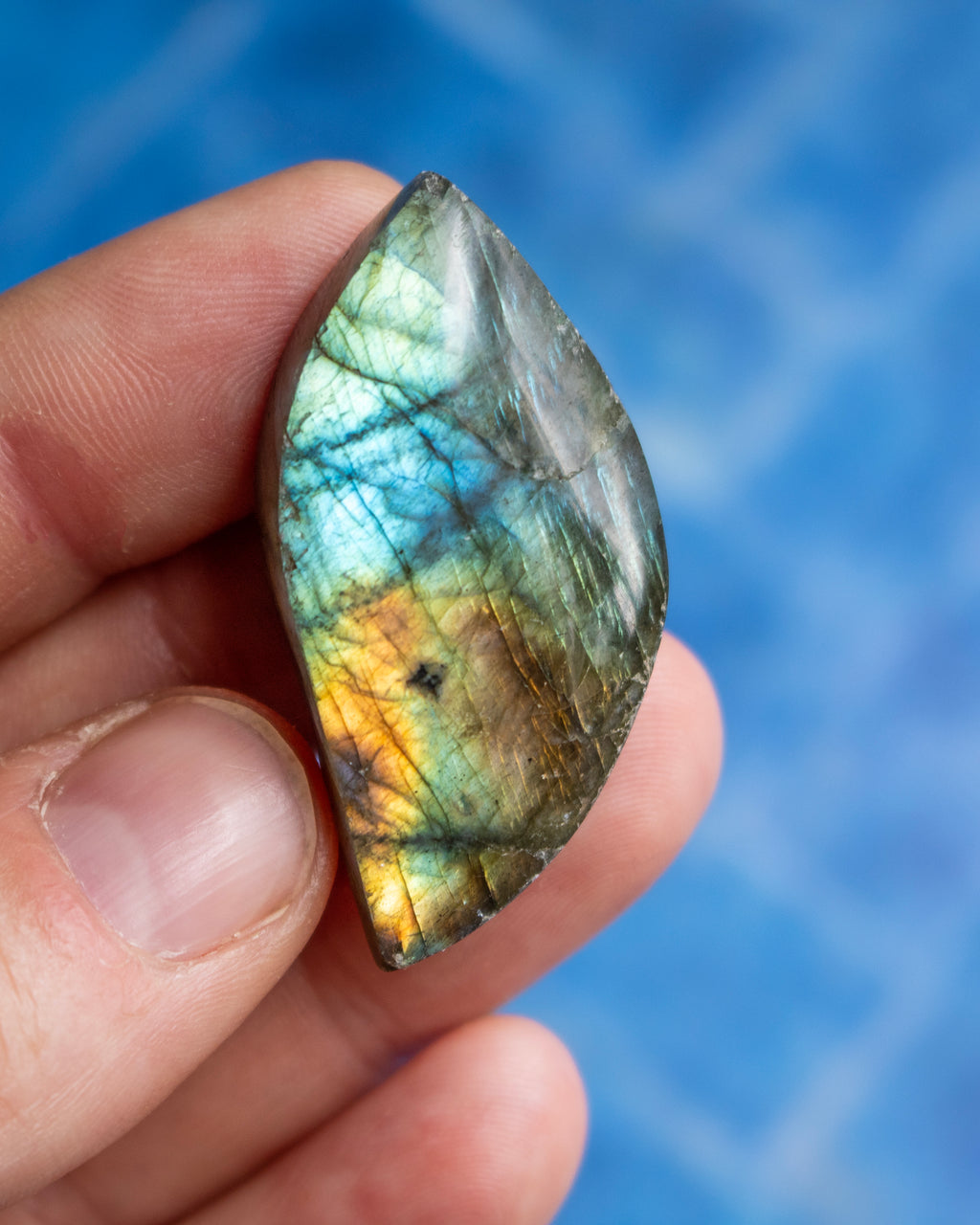 A polished labradorite stone pendant held in a person's hand against a textured blue background.