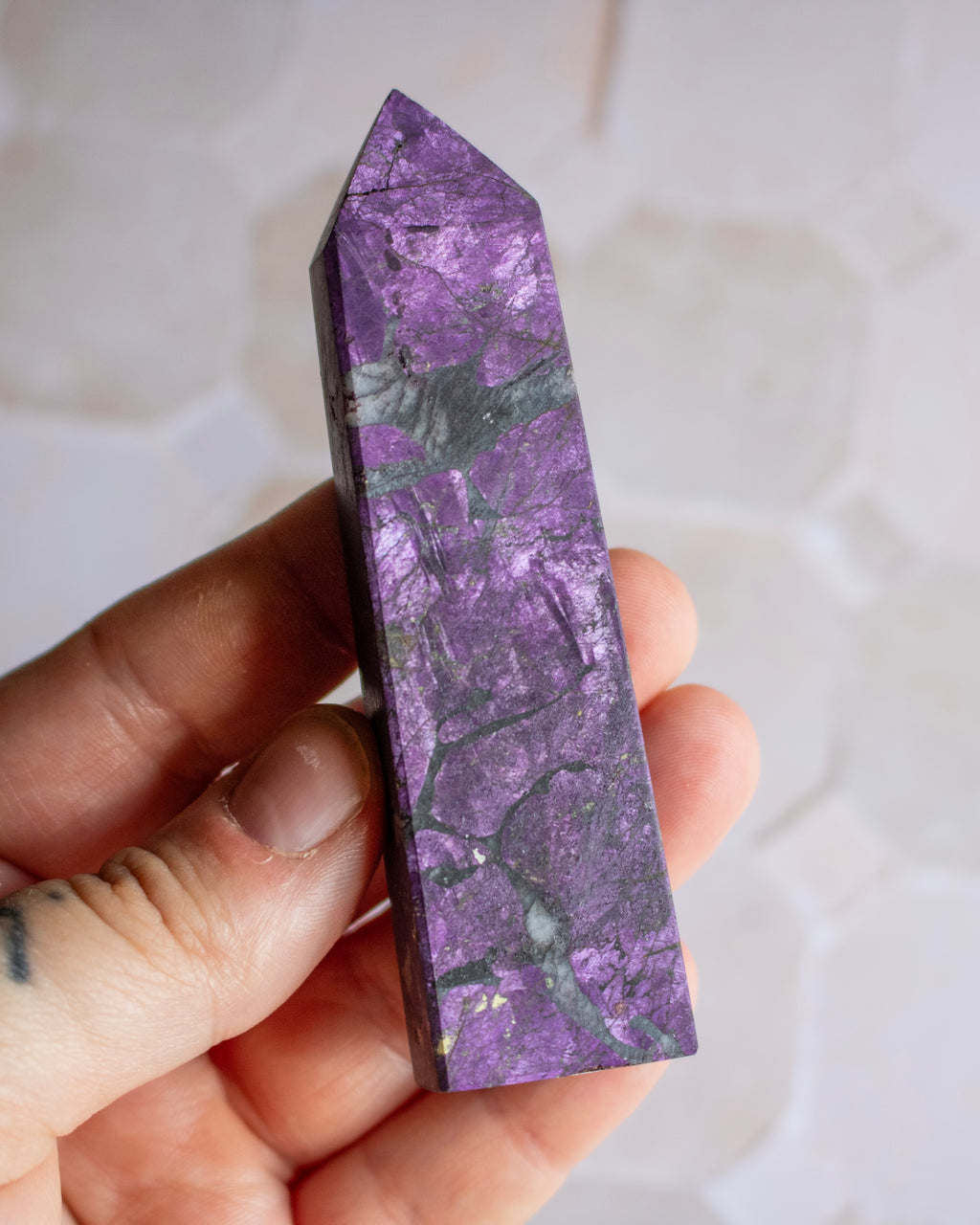 A polished purple crystal point held in a person's hand against a soft, light-colored blurred background.