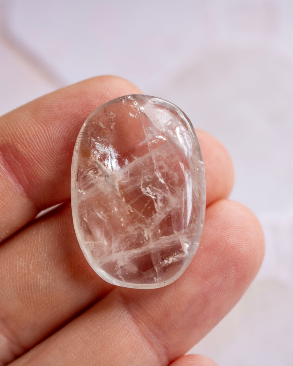 A polished oval clear quartz cabochon with visible internal crystalline structures, held in a person's fingers against a soft light background.