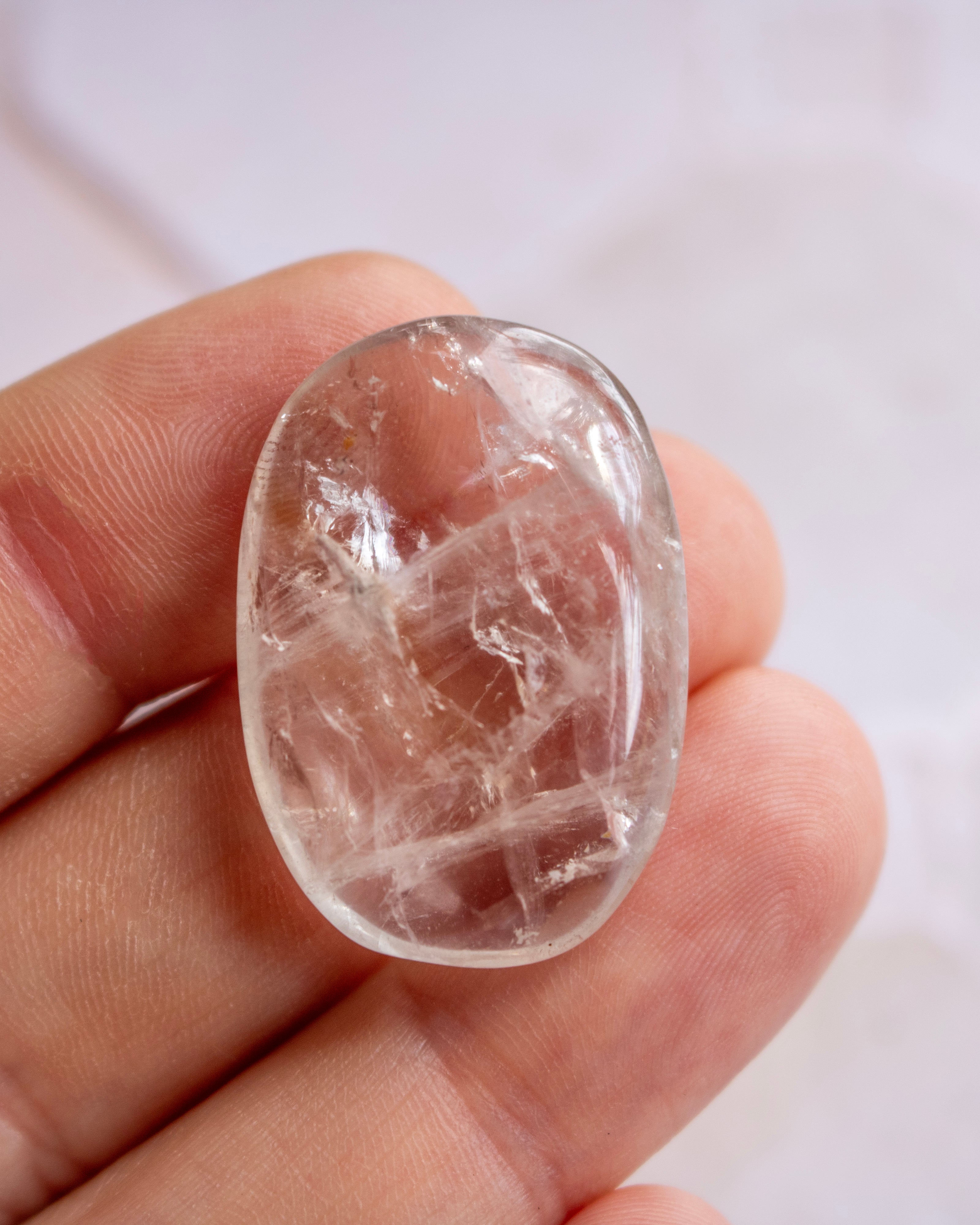 A polished oval clear quartz cabochon with visible internal crystalline structures, held in a person's fingers against a soft light background.
