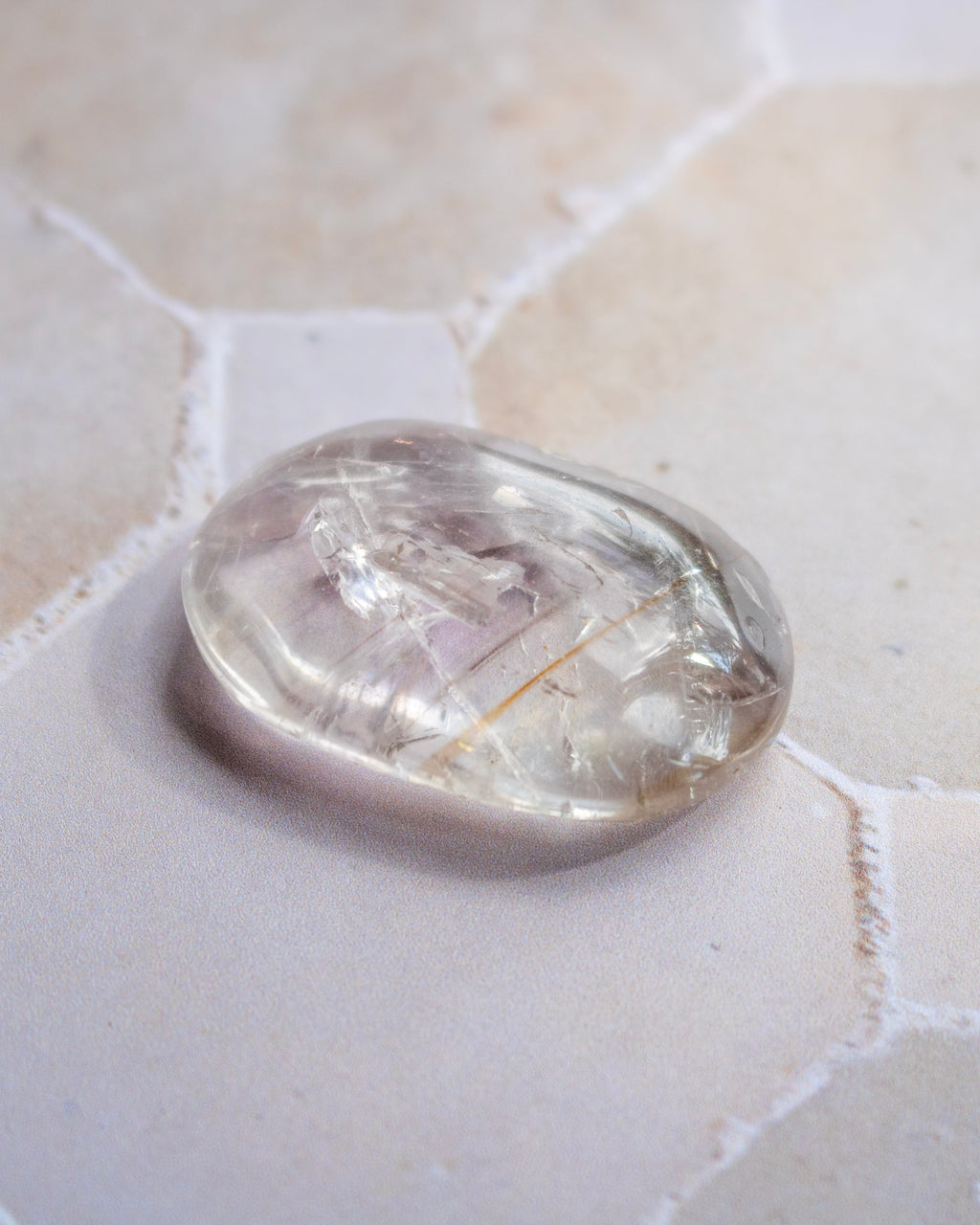 A polished, oval-shaped clear quartz crystal stone resting on a light beige stone surface.