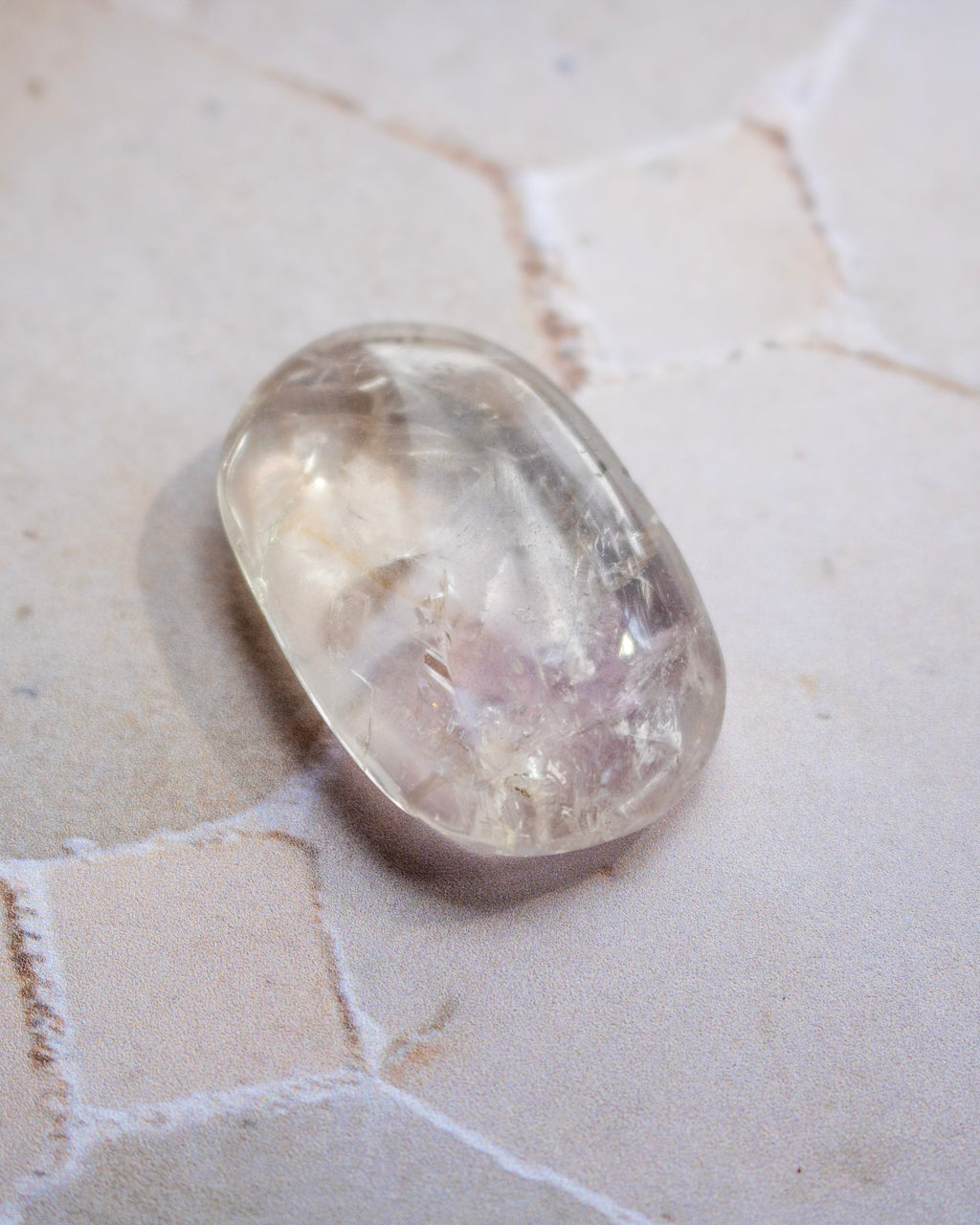 A polished oval-shaped clear gemstone with natural internal inclusions, resting on a light beige textured stone surface.