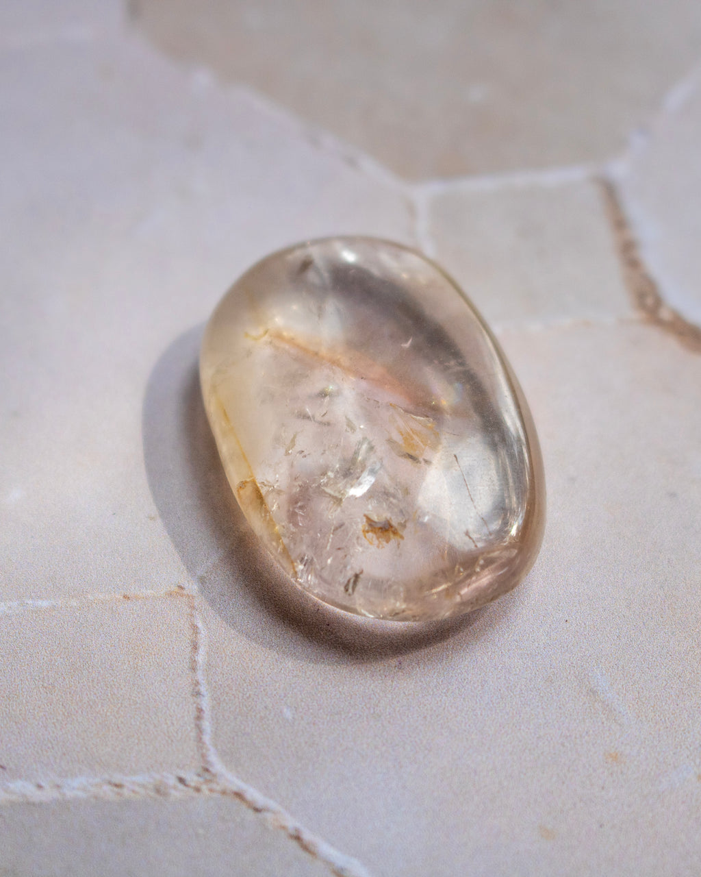 A polished, smooth oval-shaped clear gemstone with natural inclusions, resting on a light beige stone surface.