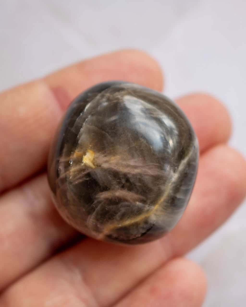 A polished dark brown gemstone with natural inclusions held in a person's hand against a light background.