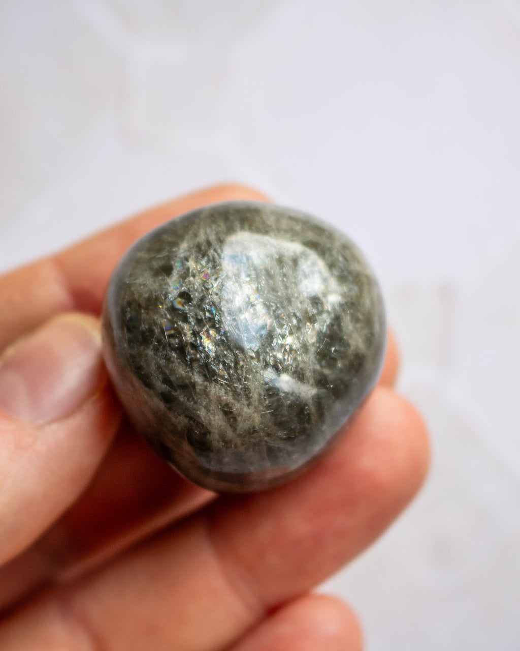 A polished dark gray stone held between fingers against a light, softly blurred background.