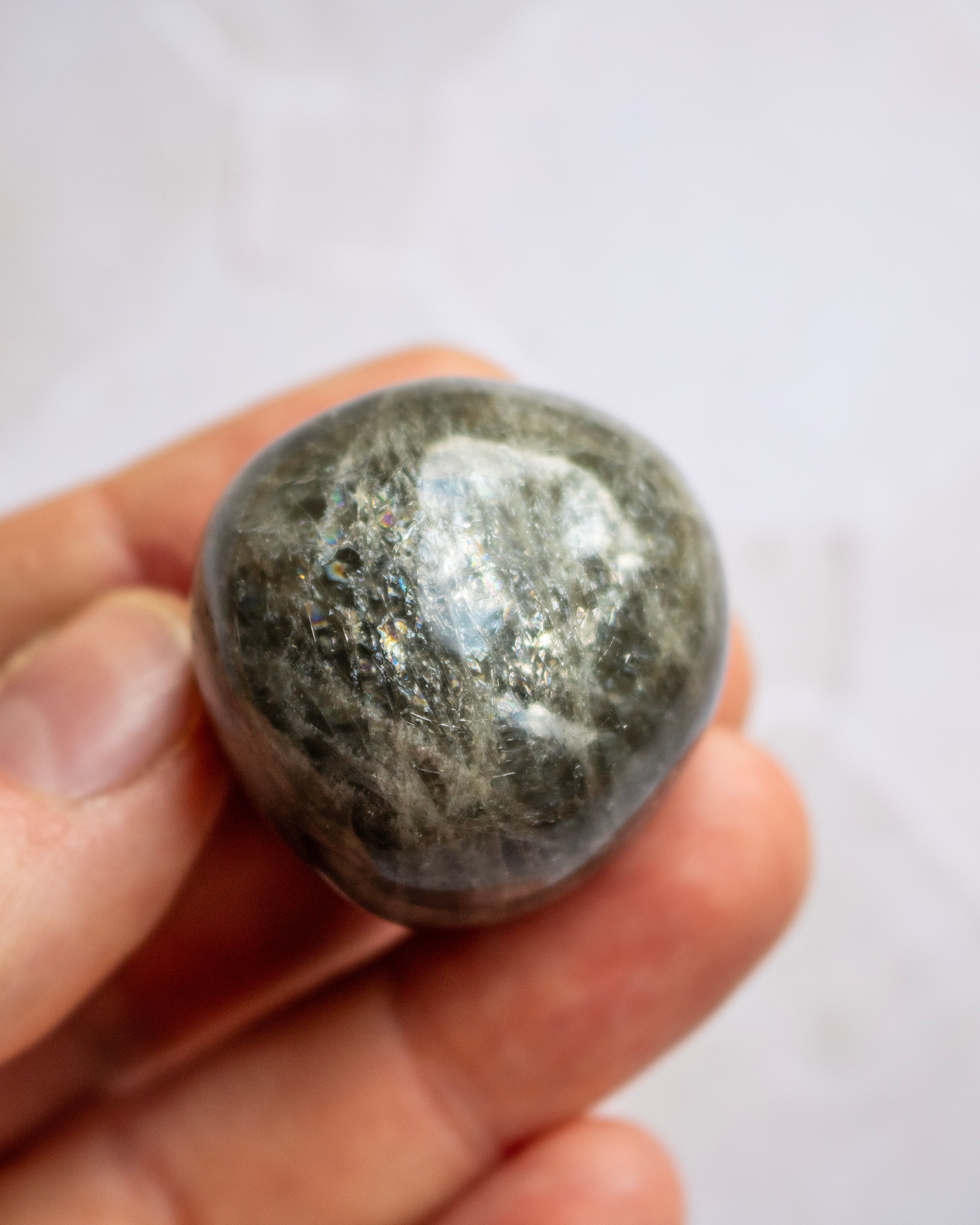 A polished dark gray stone held between fingers against a light, softly blurred background.