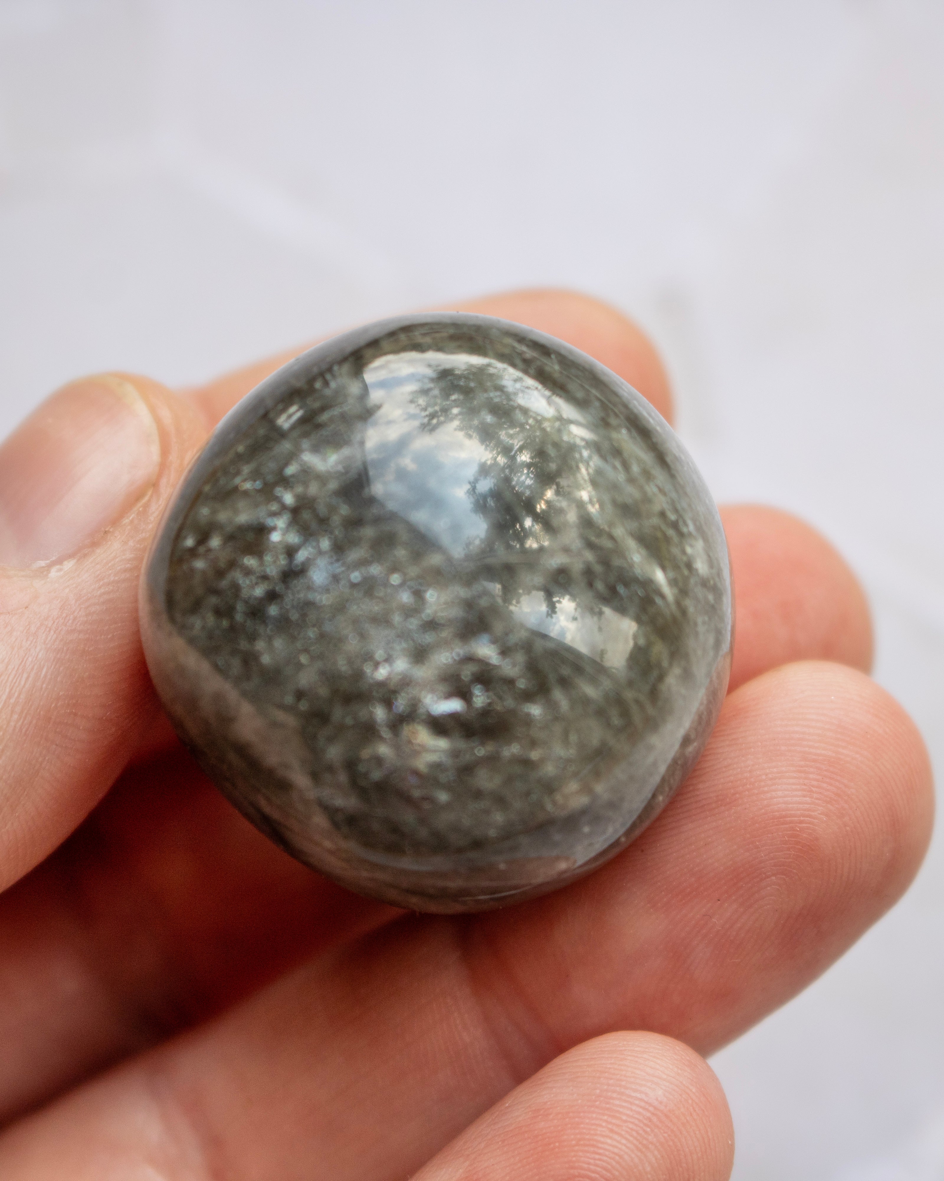 A polished gray stone sphere held in a person's hand against a light gray background.
