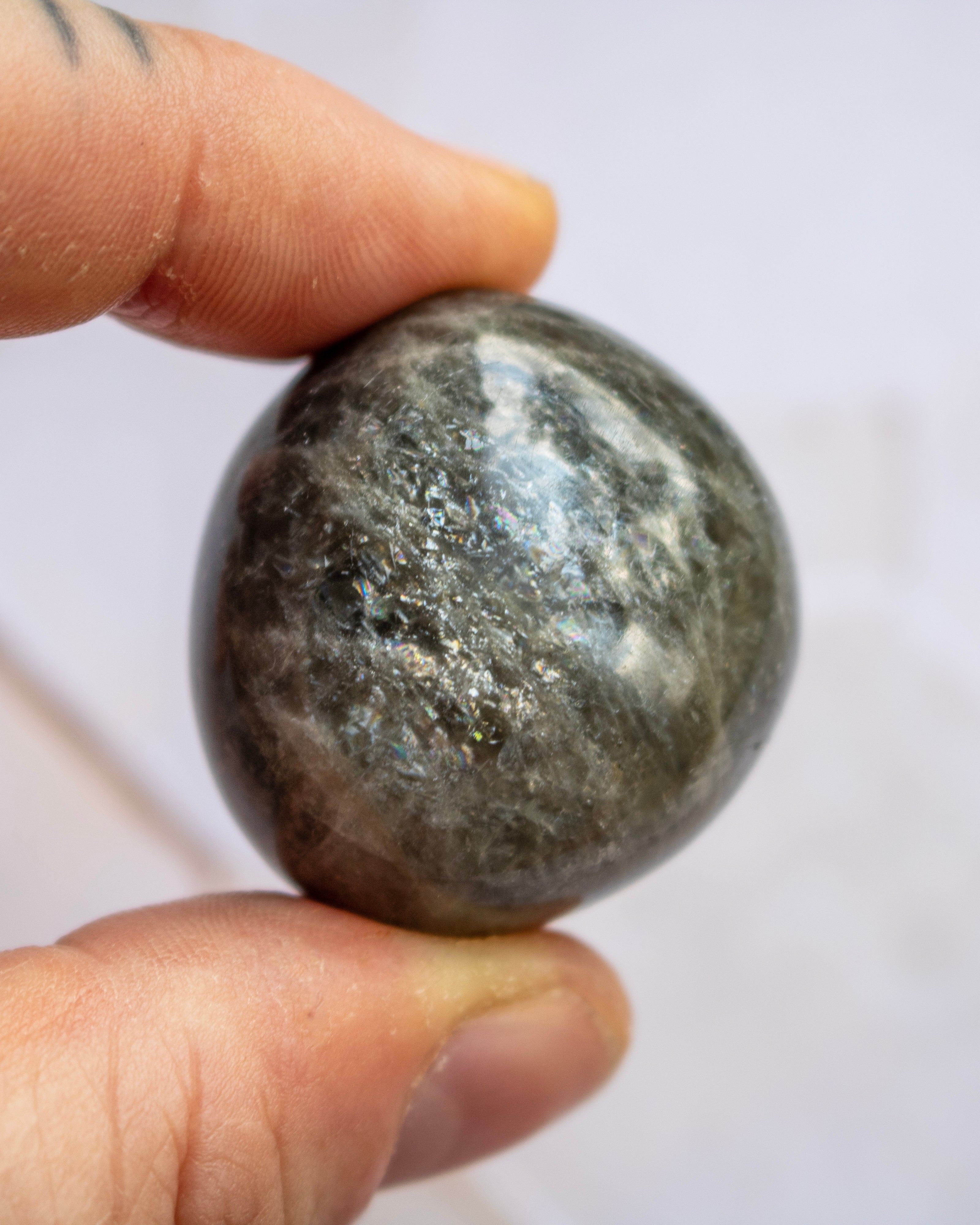 A polished dark gray stone sphere held between two human fingers against a plain light background.