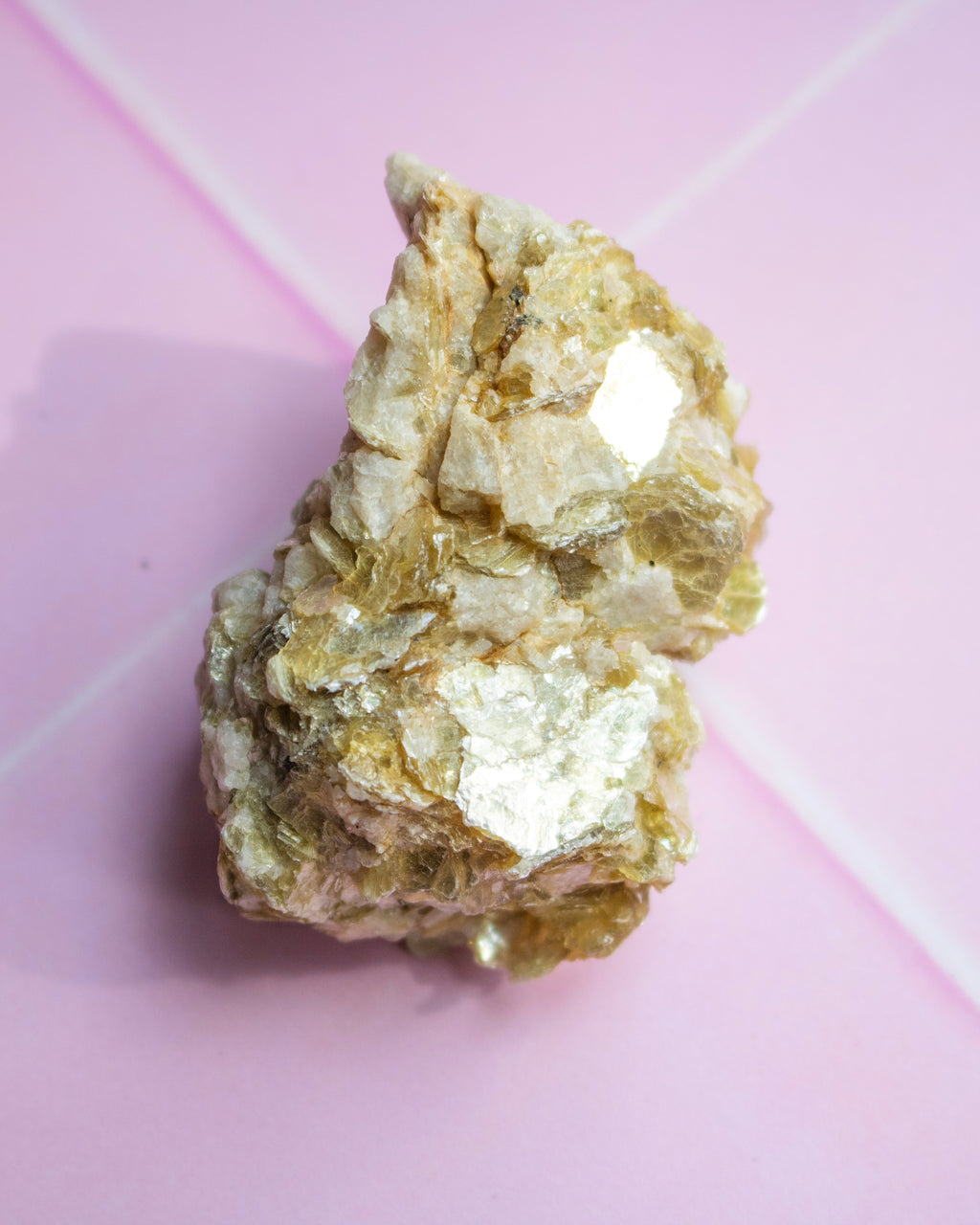 A rough, metallic gold crystal cluster with silver-toned facets, photographed on a soft pink background.