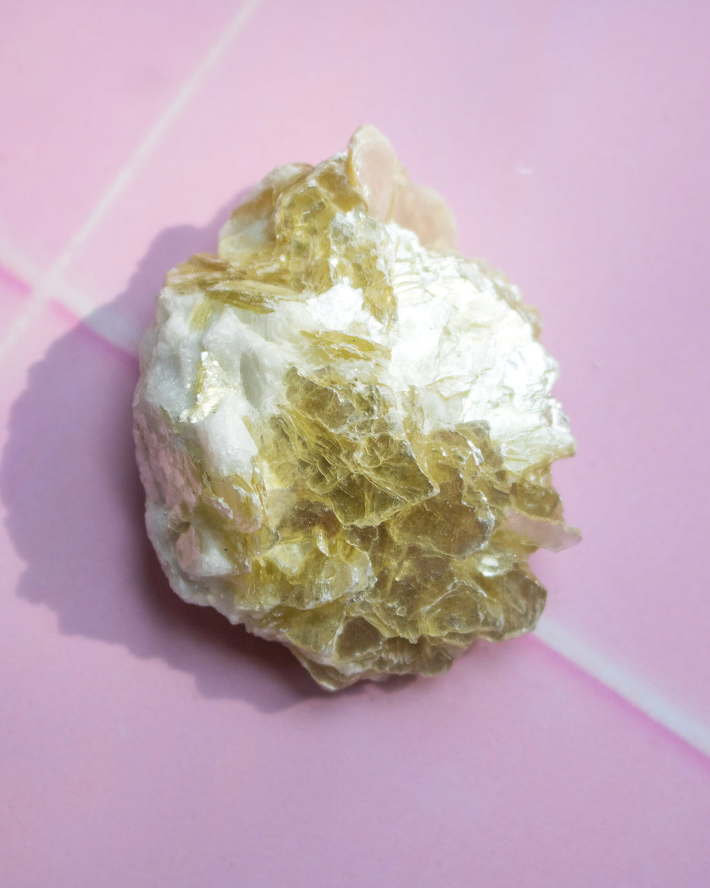 A raw, rough crystal specimen with a mix of white and translucent golden-yellow tones, resting on a pink background.