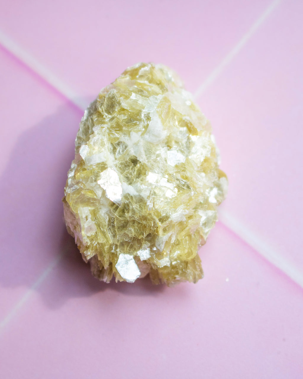 A rough, pale yellow crystalline mineral or gemstone specimen photographed on a soft pink background.