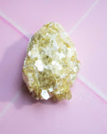 A rough, pale yellow crystalline mineral or gemstone specimen photographed on a soft pink background.