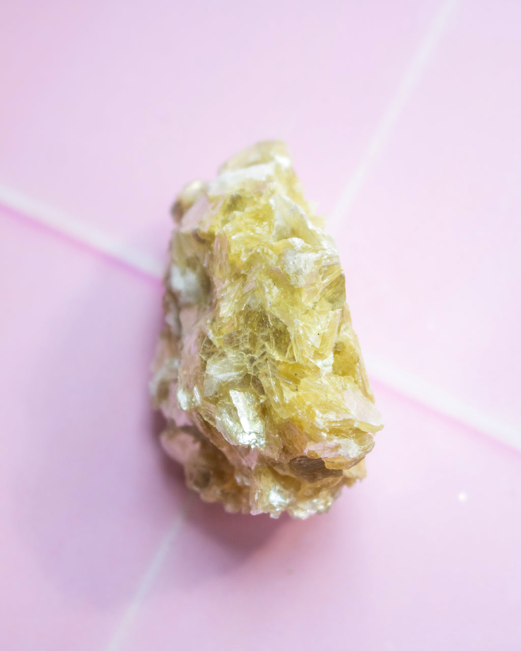 A rough, pale yellow crystalline mineral or gemstone specimen photographed on a soft pink background.