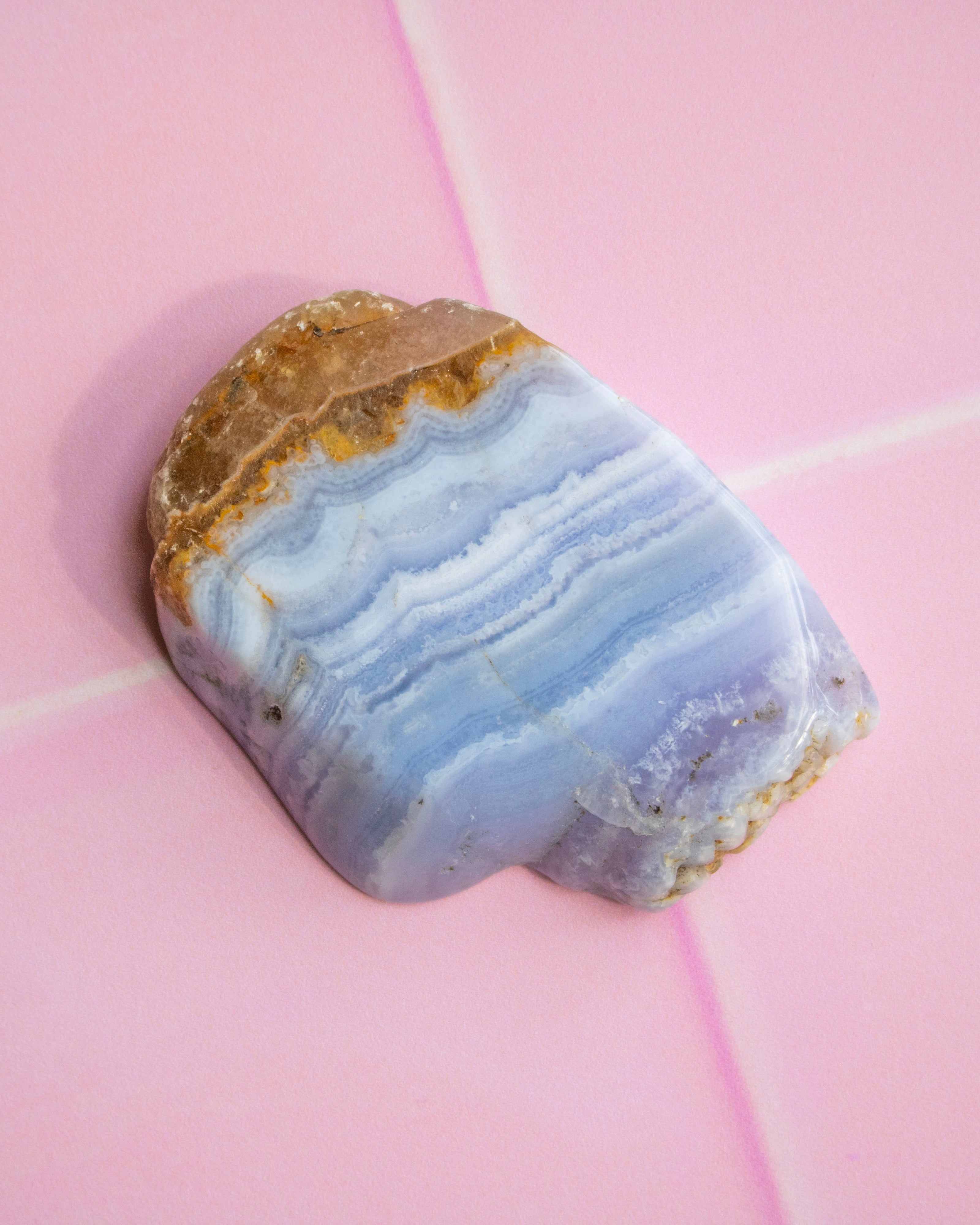 A polished stone slice with layered light blue, lavender, and white bands, resting on a pink tiled surface.