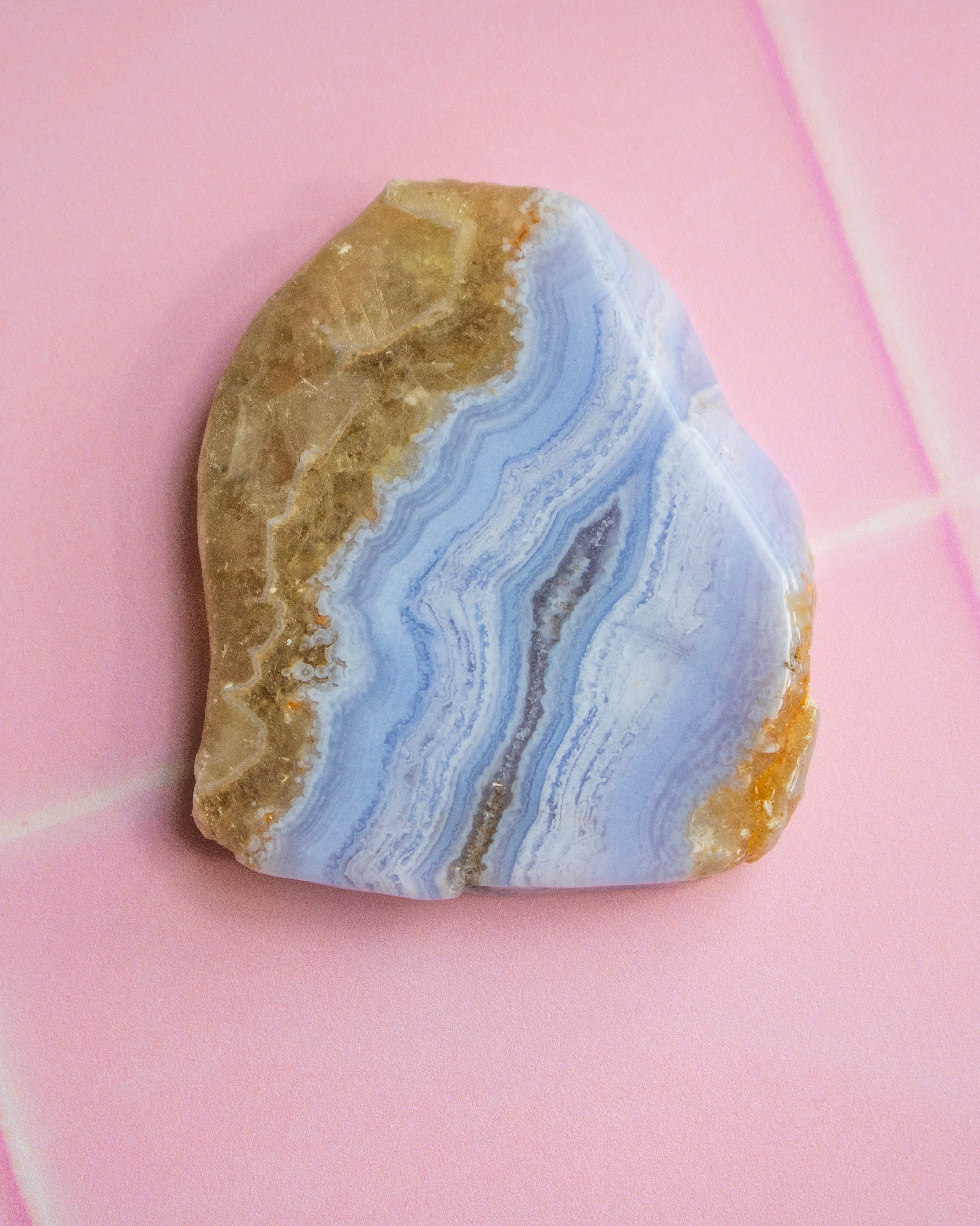 A polished natural stone with wavy bands of light blue, white, tan, and brown, photographed on a pink background.