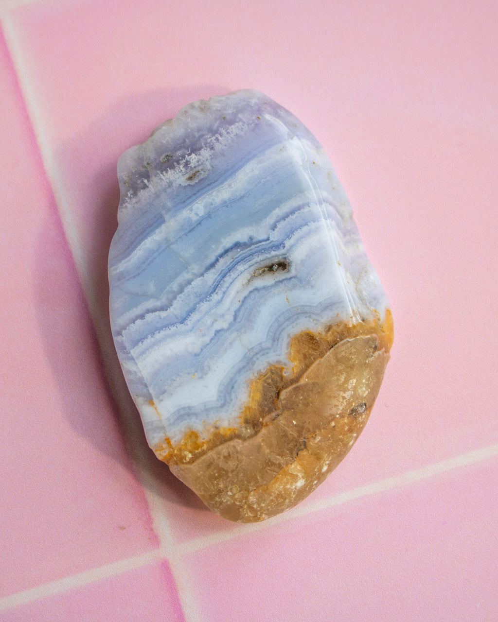 A polished natural stone with wavy bands of light blue, white, and tan, resting on a pink tiled surface.