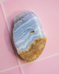 A polished natural stone with wavy bands of light blue, white, and tan, resting on a pink tiled surface.