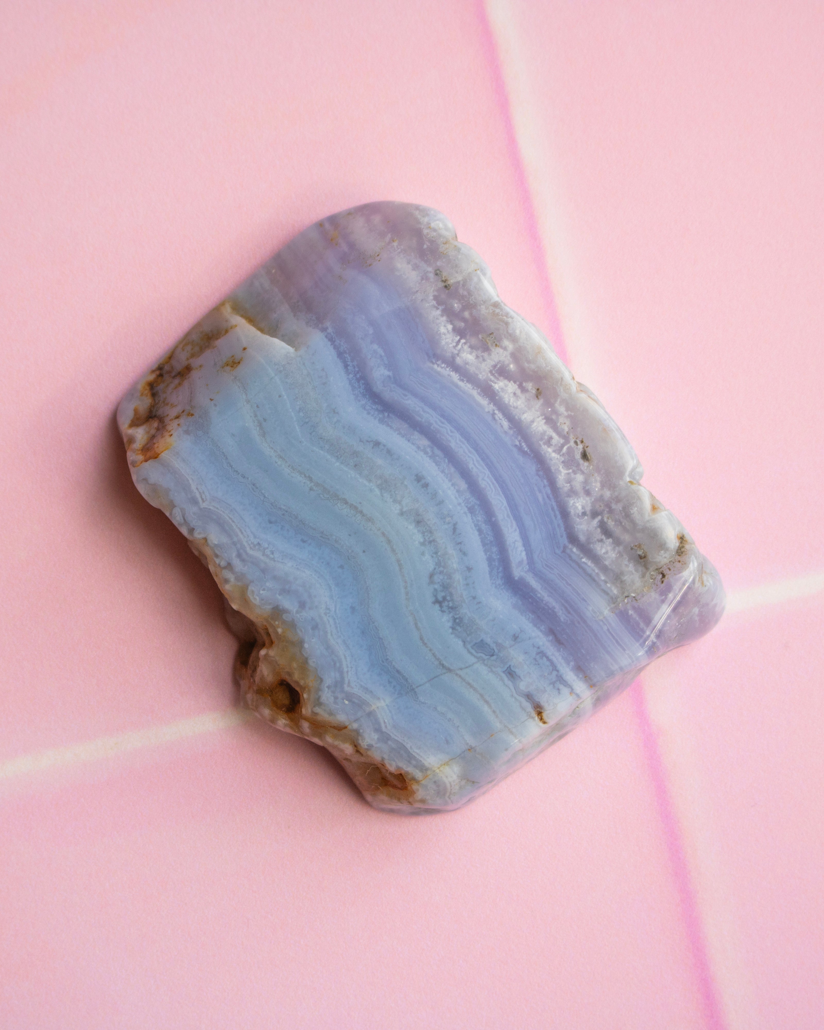A polished agate stone with layered light blue, lavender, and white bands, resting on a pink tiled surface.