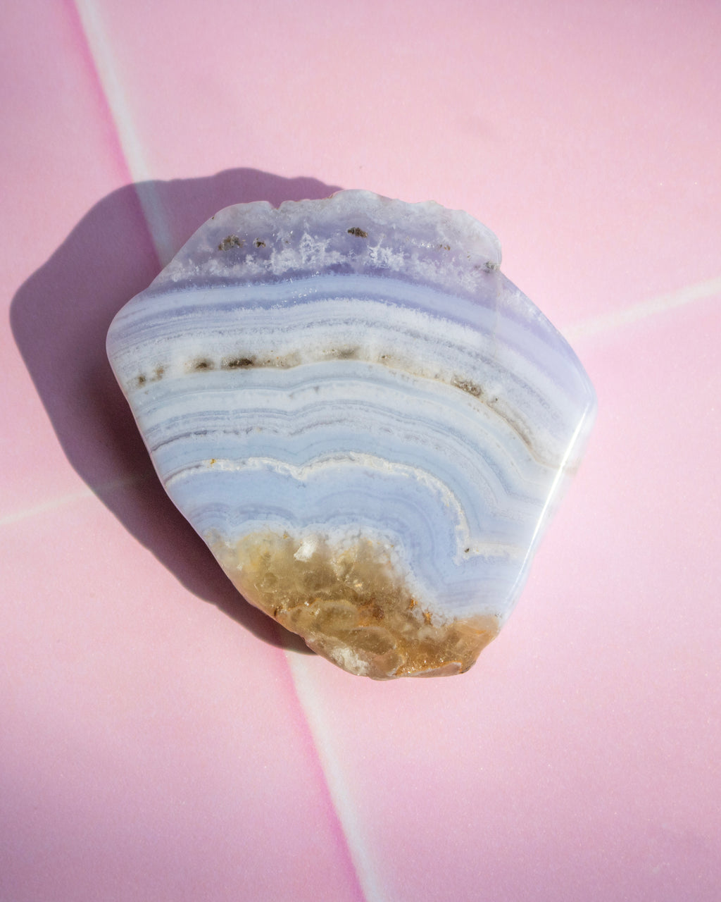 A polished agate stone with layered light blue, lavender, and white bands, resting on a pink tiled surface.