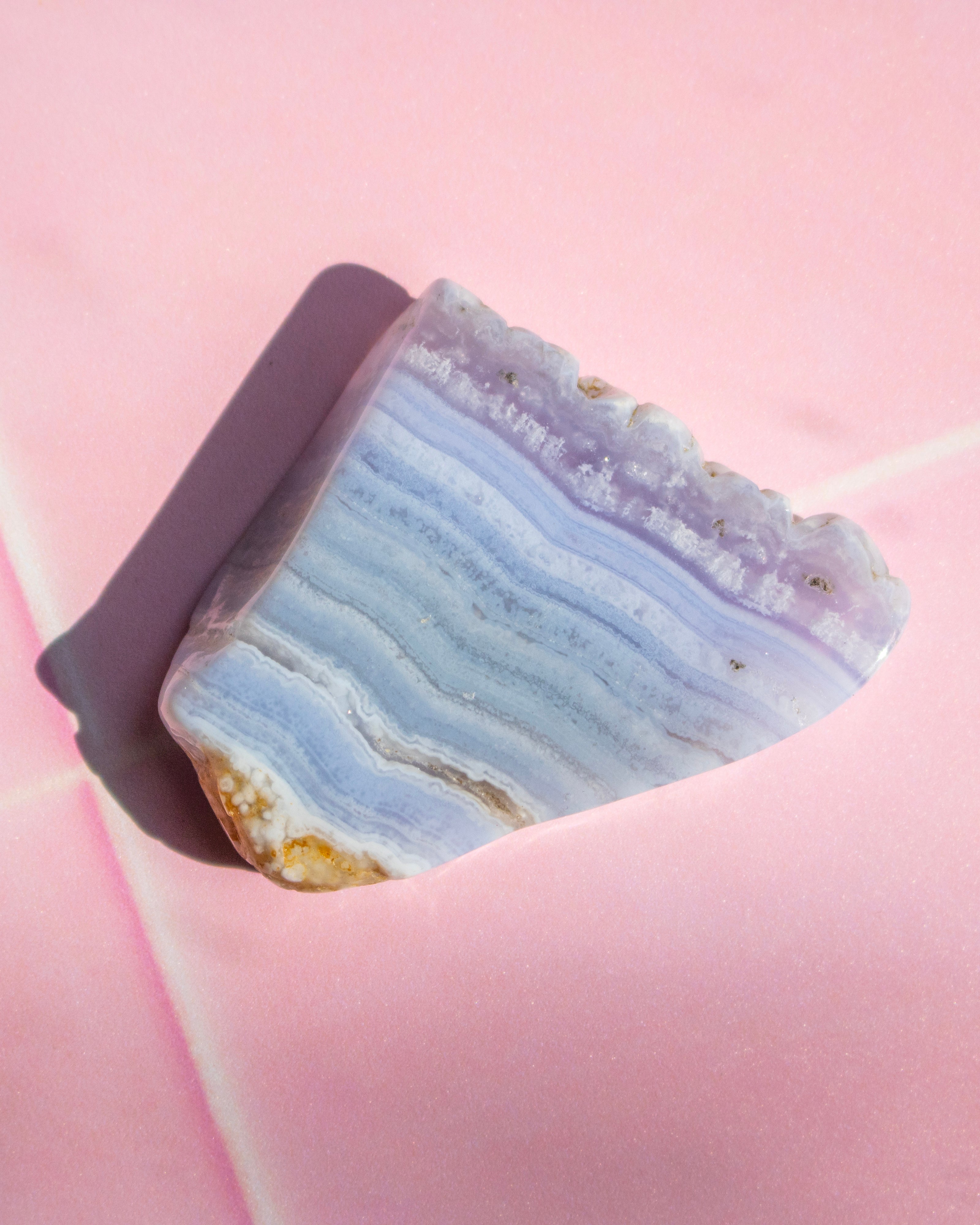 A polished slice of agate crystal with layered blue, purple, and white bands, resting on a soft pink background.