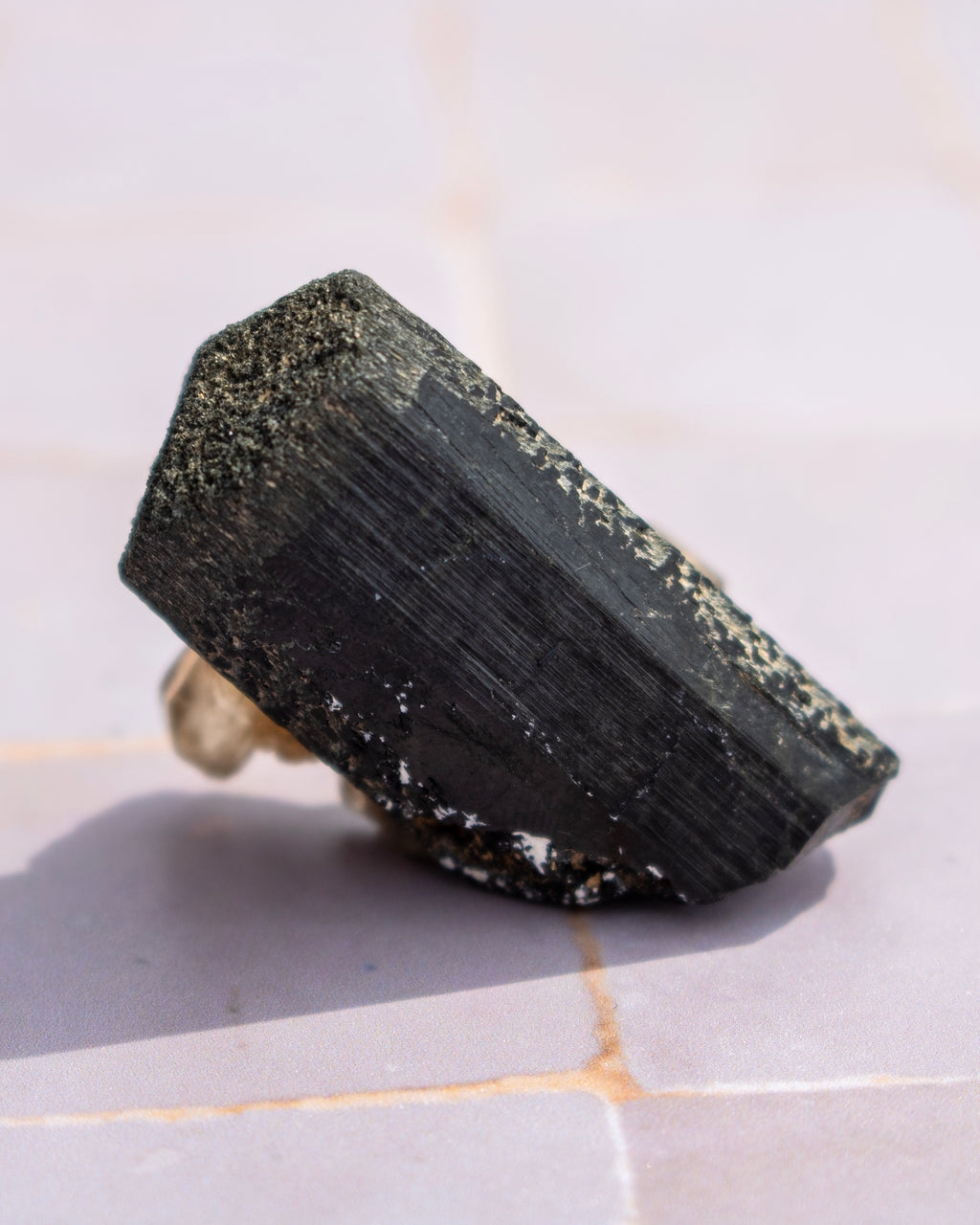 A raw black tourmaline crystal with a hexagonal shape, resting on a light-colored tiled surface.
