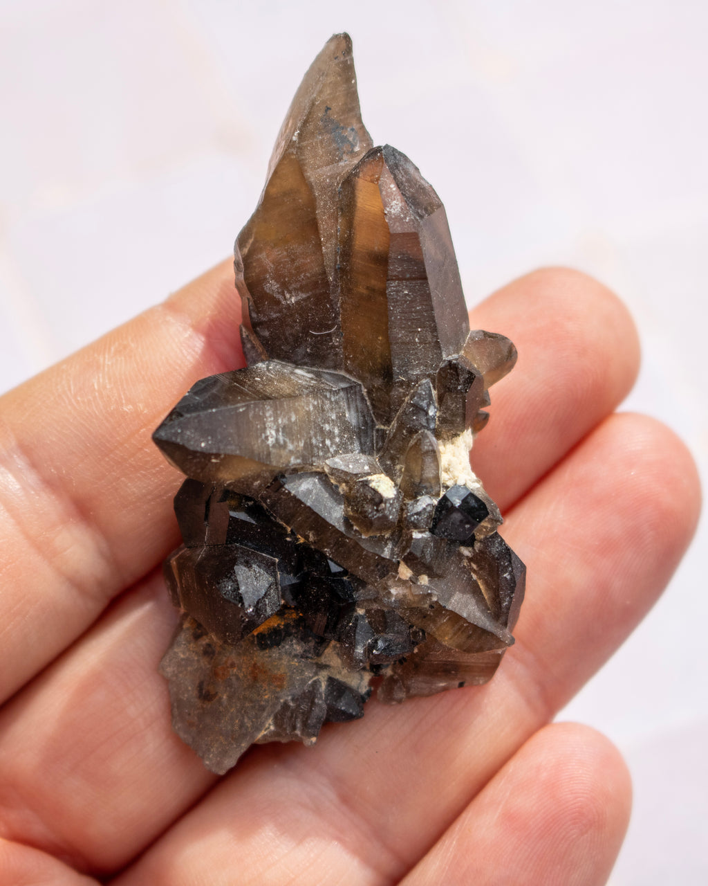 A raw smoky quartz crystal cluster held in a person's hand against a light, out-of-focus background.