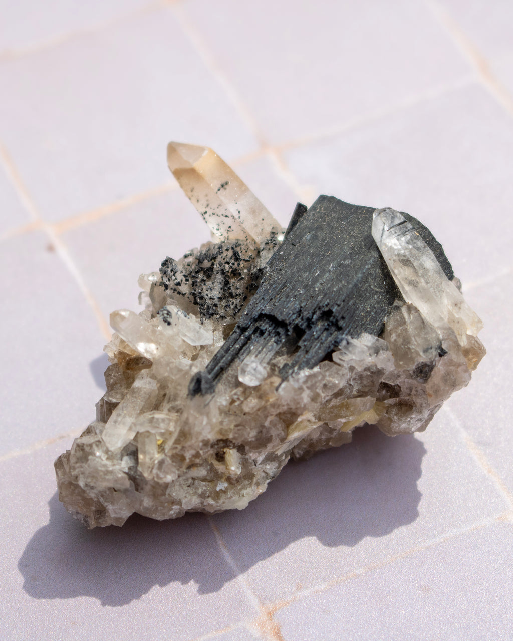 A natural mineral specimen featuring clear quartz crystal points and a prominent dark gray to black metallic mineral section, resting on a light gray tiled surface.