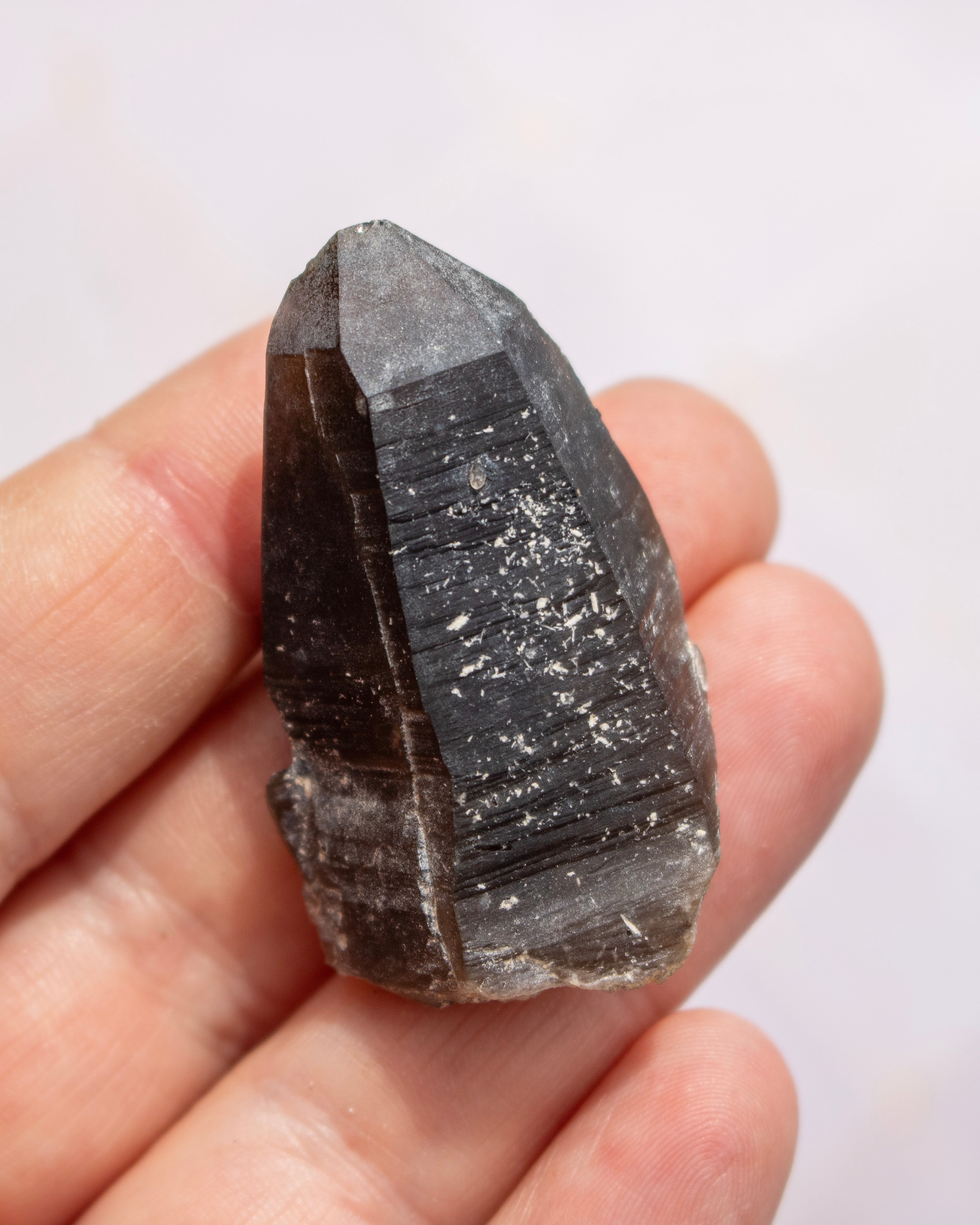 A raw smoky quartz crystal point held in a person's hand against a plain light background.