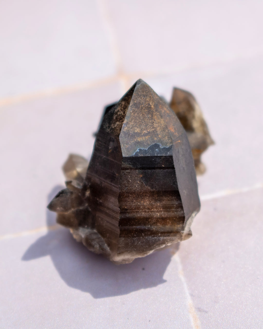 A natural smoky quartz crystal cluster with a prominent pointed central tip, resting on a light-colored tiled surface.