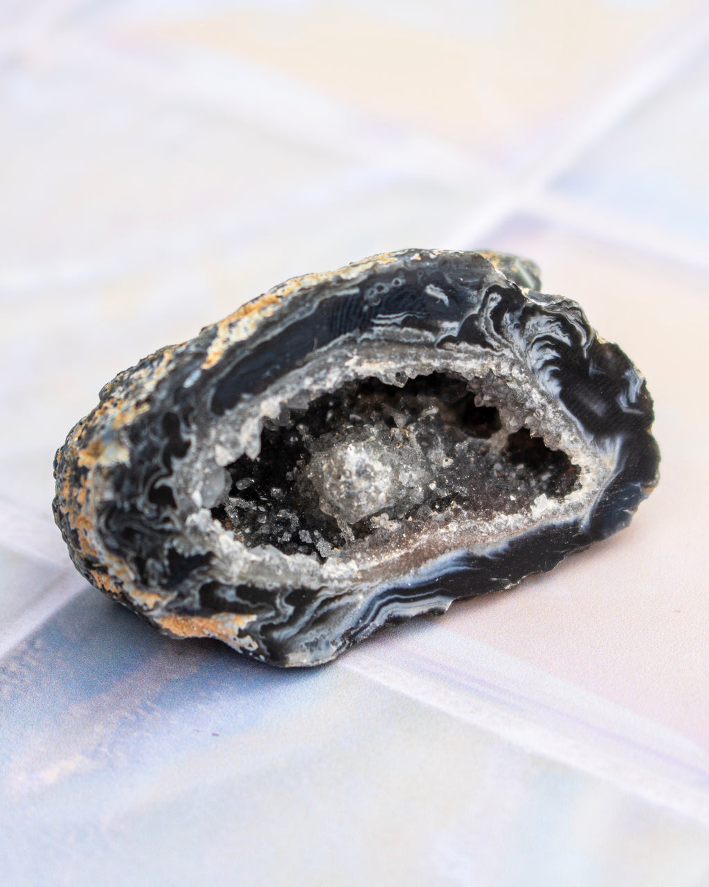 A polished geode slice with a dark black outer matrix and a bright white crystal cavity, resting on a light iridescent surface.