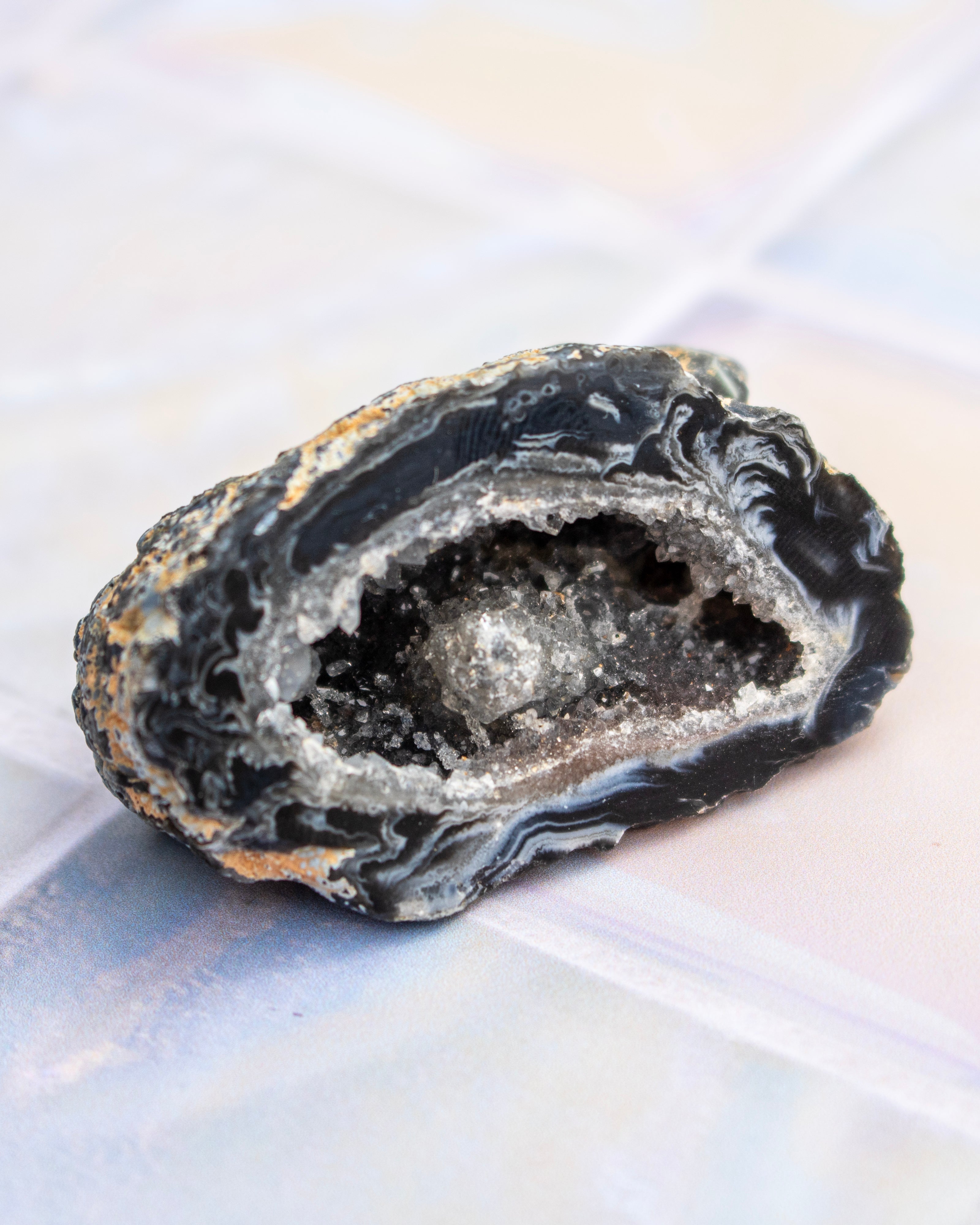 A polished geode slice with a dark black outer matrix and a bright white crystal cavity, resting on a light iridescent surface.