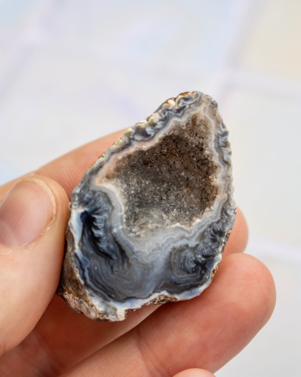 A hand holding a polished natural geode or agate dome with a dark gray crystalline center and layered gray, white, and black outer bands.