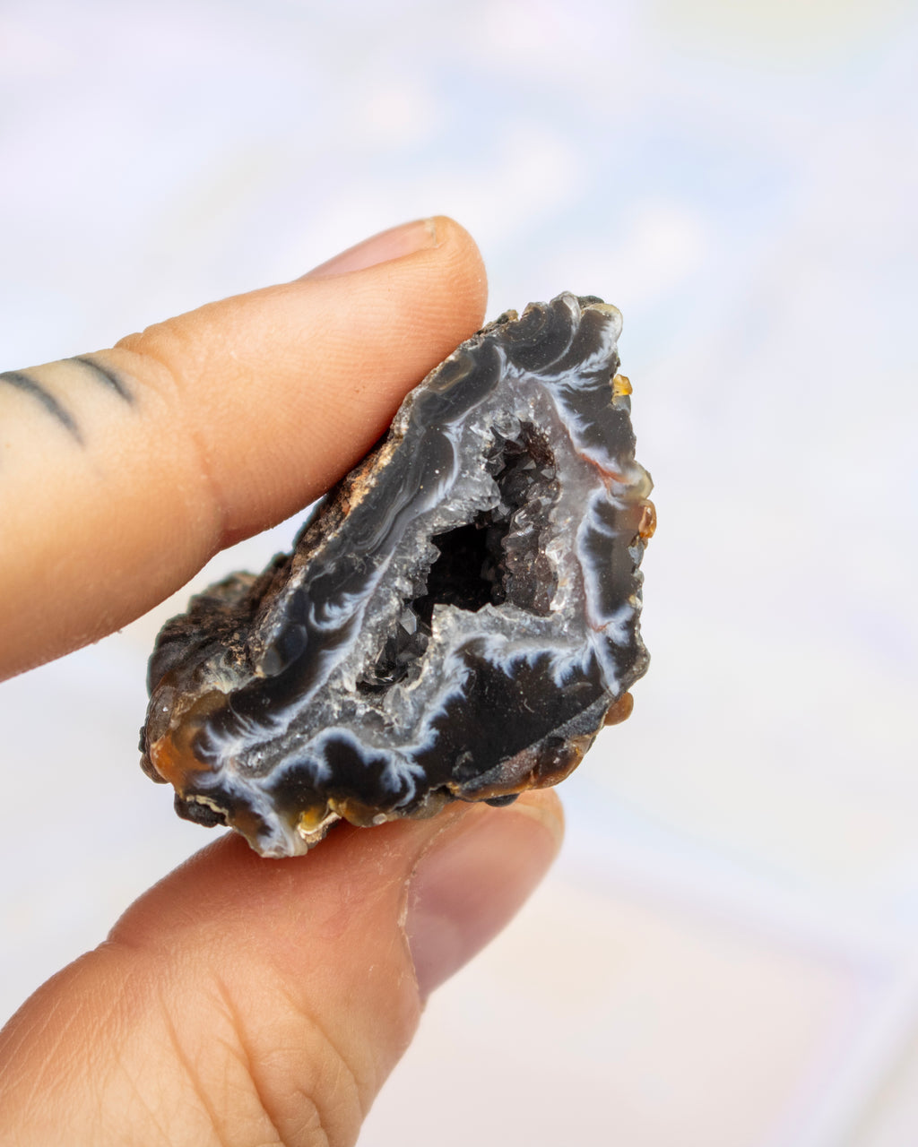 A hand holding a polished natural agate geode slice showing dark black and gray outer layers with white banded inner patterns.