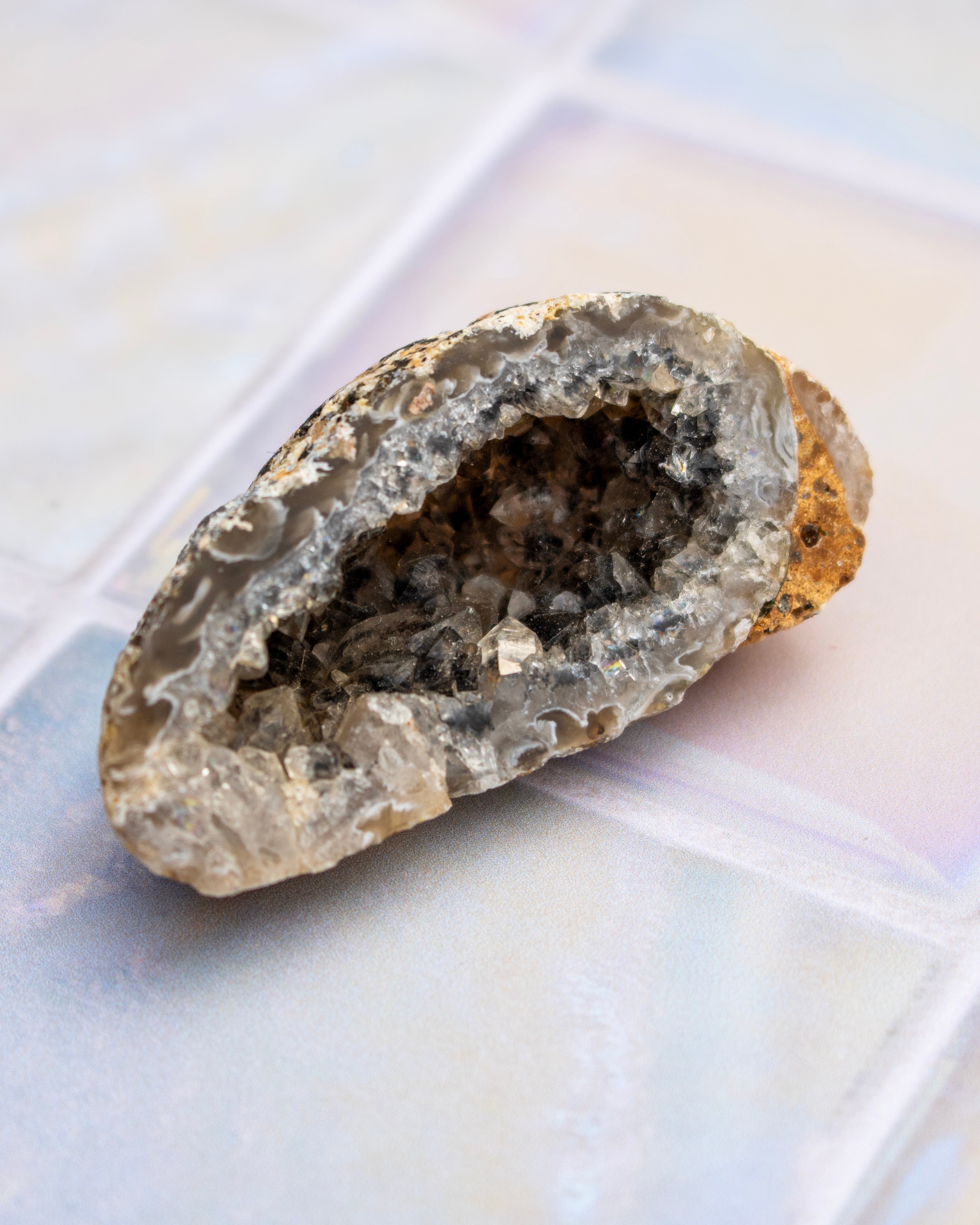 A natural geode specimen with a hollowed-out cavity filled with gray and white crystalline formations, resting on a light-colored tiled surface.