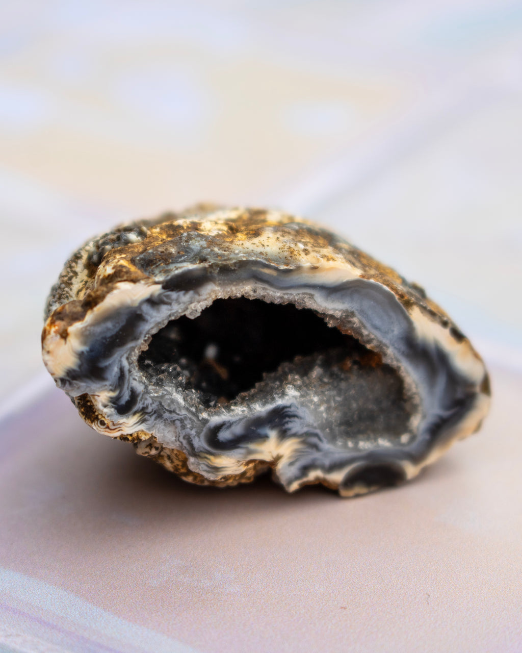 A polished geode slice with a dark gray to black outer layer and a bright white crystal cavity interior, resting on a soft beige surface.