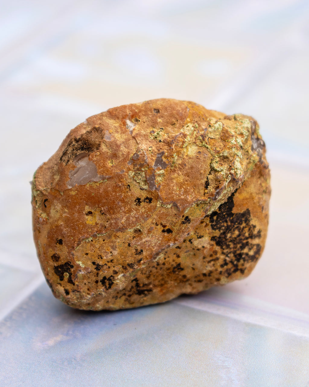 A rough, polished brown and gold mineral specimen with dark speckles, photographed on a light-colored, subtly reflective surface.