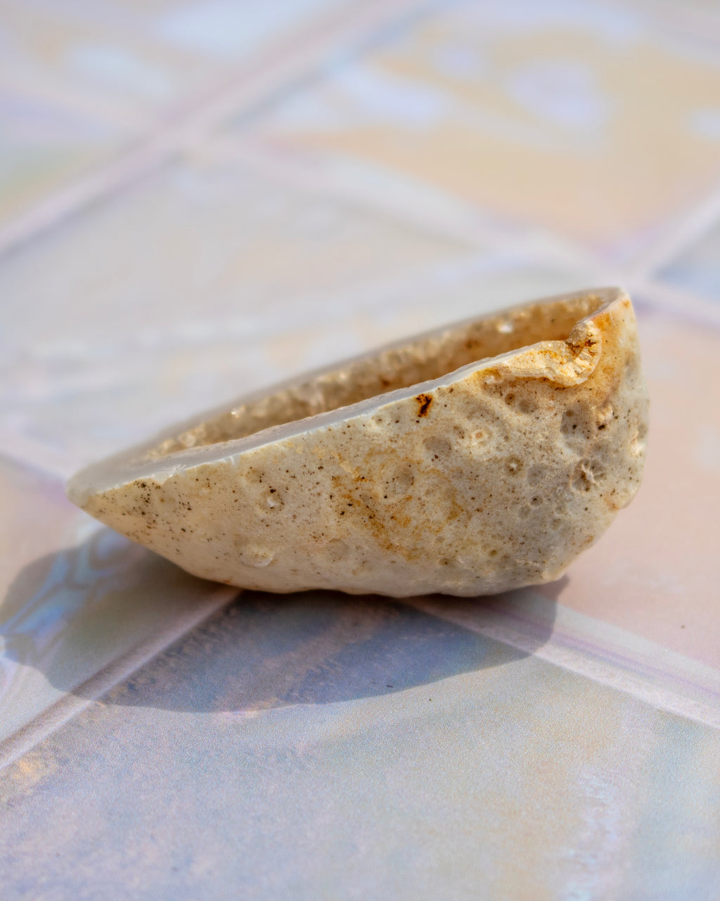 A natural porous geode, displayed on a glossy, iridescent tile surface.