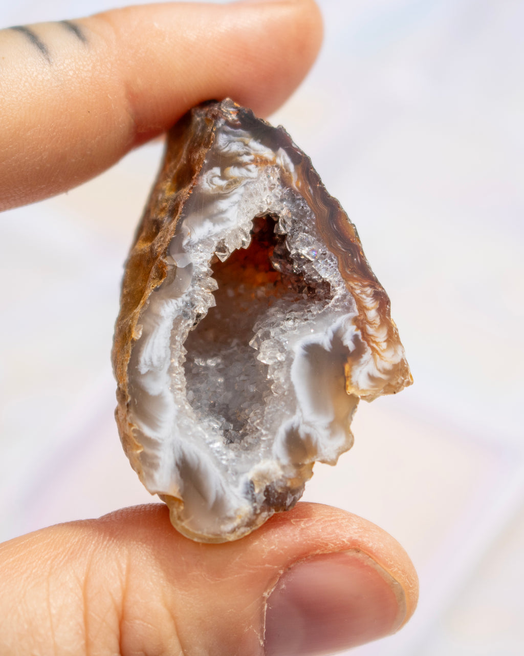 A close-up of a hand holding a polished agate geode cavity with a white crystal interior and brown outer edges.