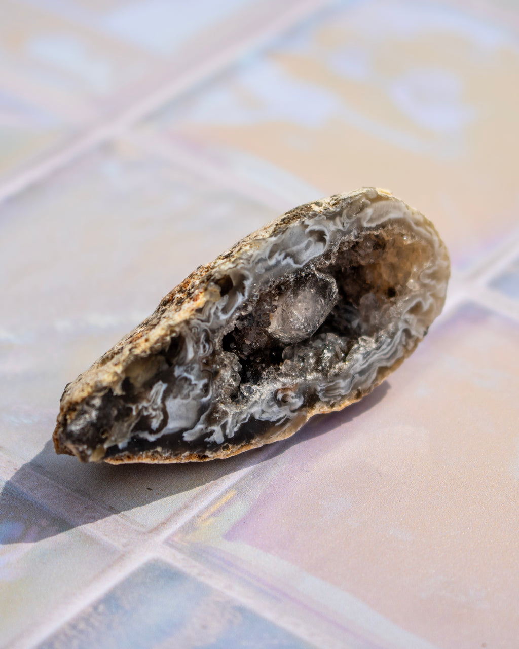 A natural geode specimen with a rough, textured outer shell and a crystalline interior, resting on a tiled surface.