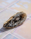 A natural geode specimen with a rough, textured outer shell and a crystalline interior, resting on a tiled surface.