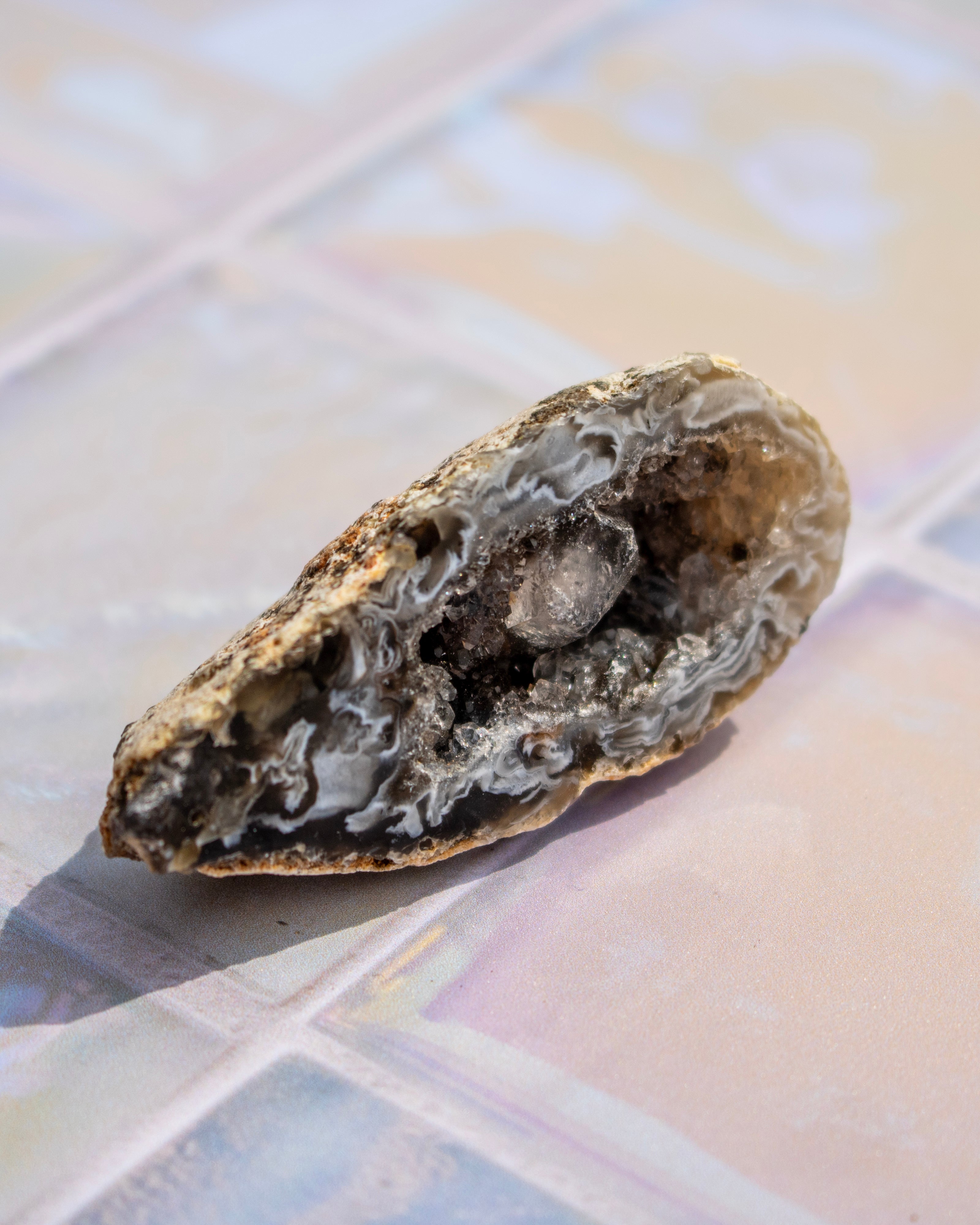 A natural geode specimen with a rough, textured outer shell and a crystalline interior, resting on a tiled surface.