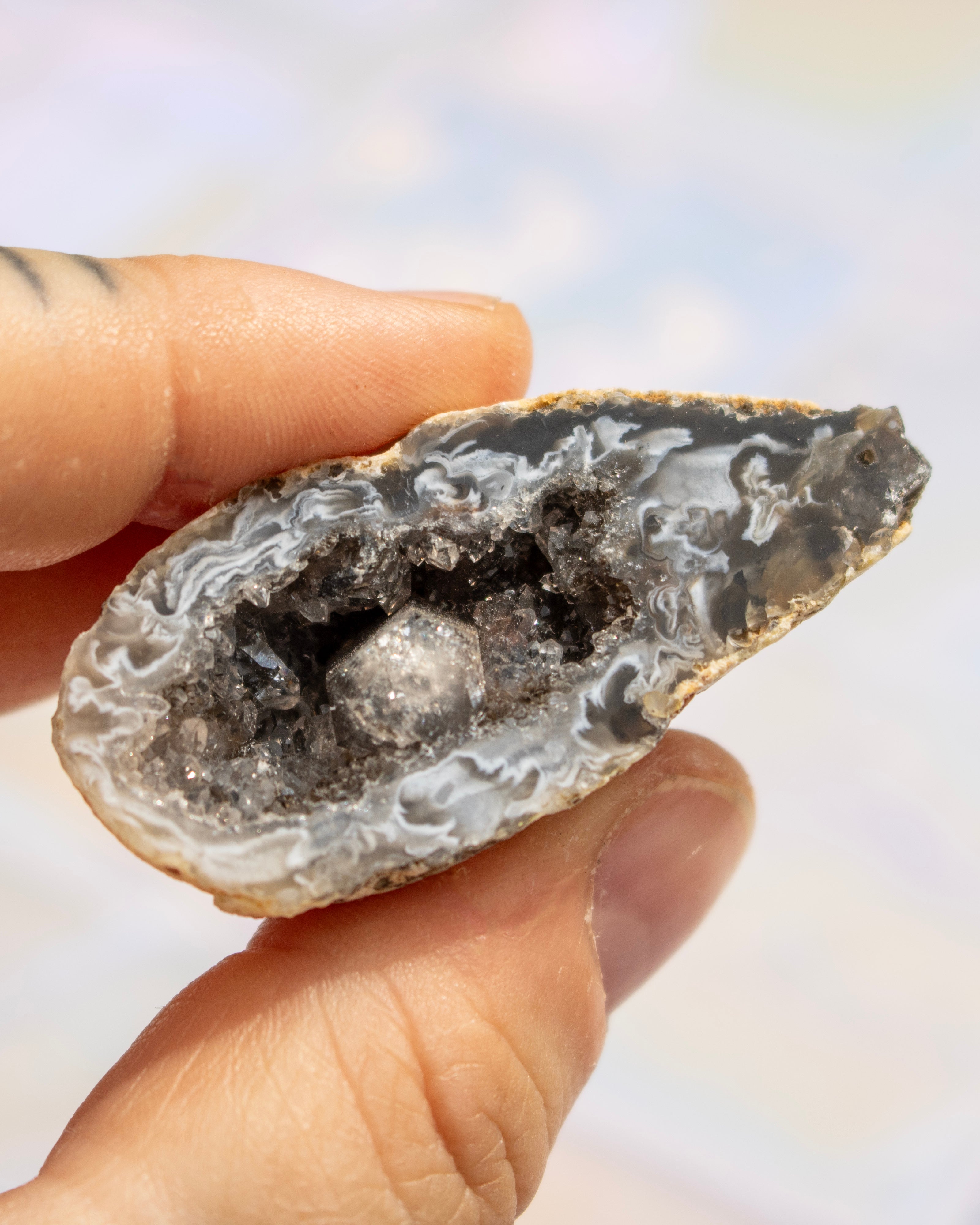 A close-up of a hand holding a cross-section of a geode specimen showing white and gray agate-like crystal formations with a darker central cavity.