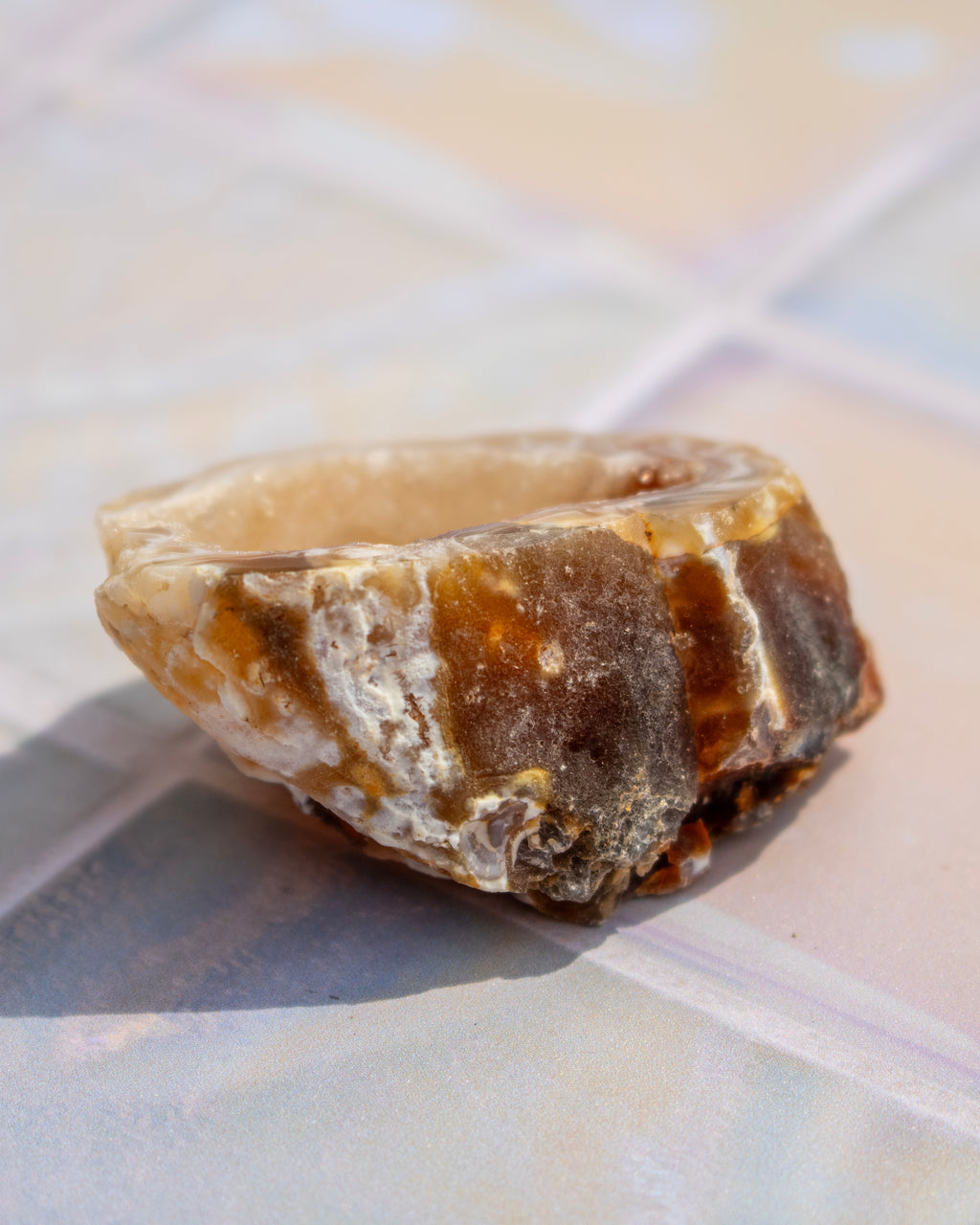 A rustic, raw stone, featuring natural textures in brown, beige, and white, resting on a tiled surface.