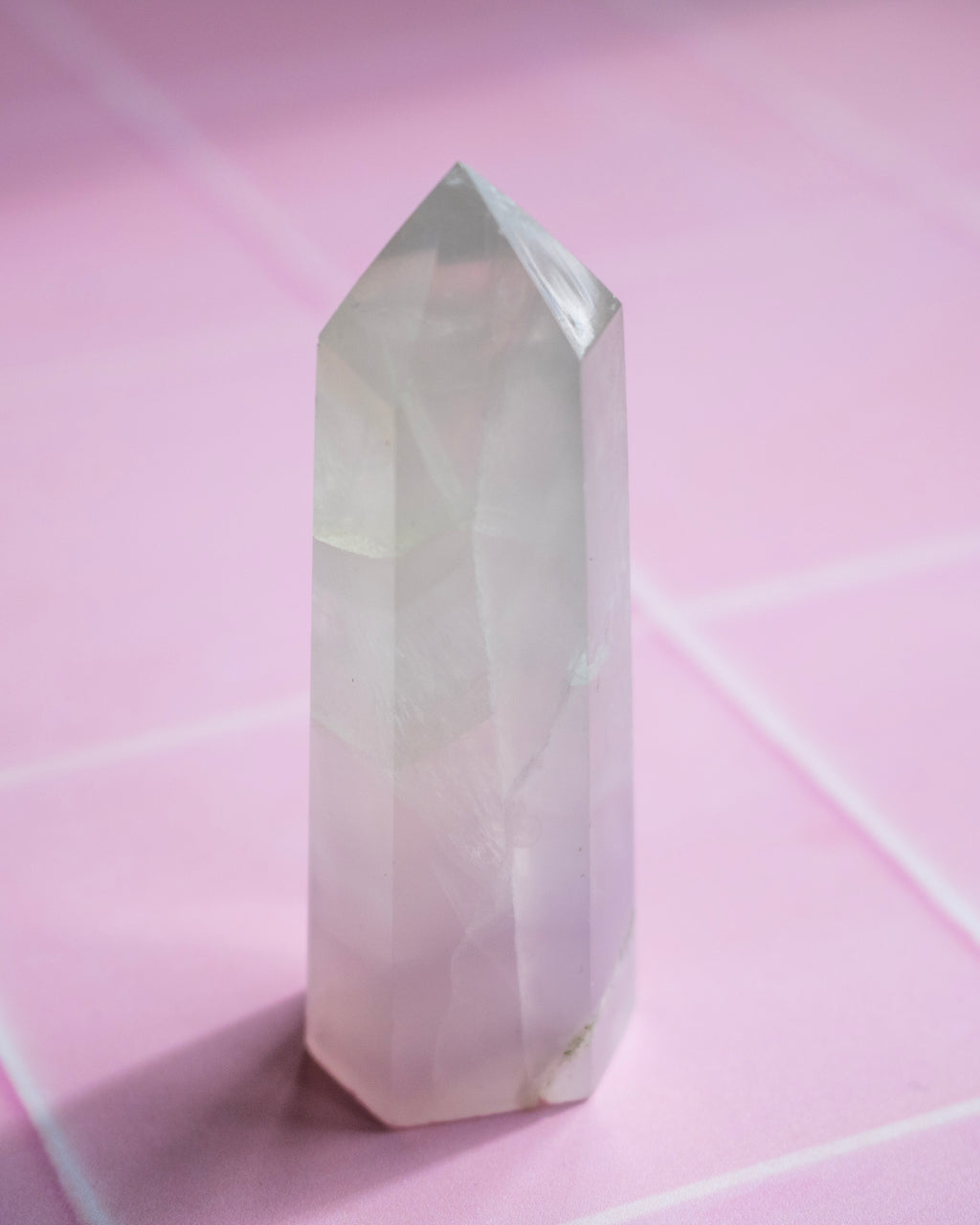 A pale pink pointed crystal tower standing upright on a pink surface with faint grid lines.